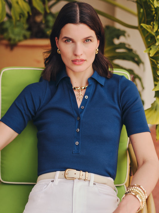 A confident woman wearing a navy Theodora Short Sleeve Shirt by J.McLaughlin, paired with white pants and gold accessories, embodying effortlessly stylish, enduring designs and a legacy of timeless fashion. A destination for defining style. Life, Well-Lived.