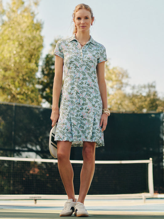 A woman stands on a tennis court wearing the Dorte Dress in Neo Blooming Vines by J.McLaughlin, featuring an effortlessly stylish floral pattern that reflects enduring designs and a legacy of timeless fashion. A destination for defining style. Life, Well-Lived.