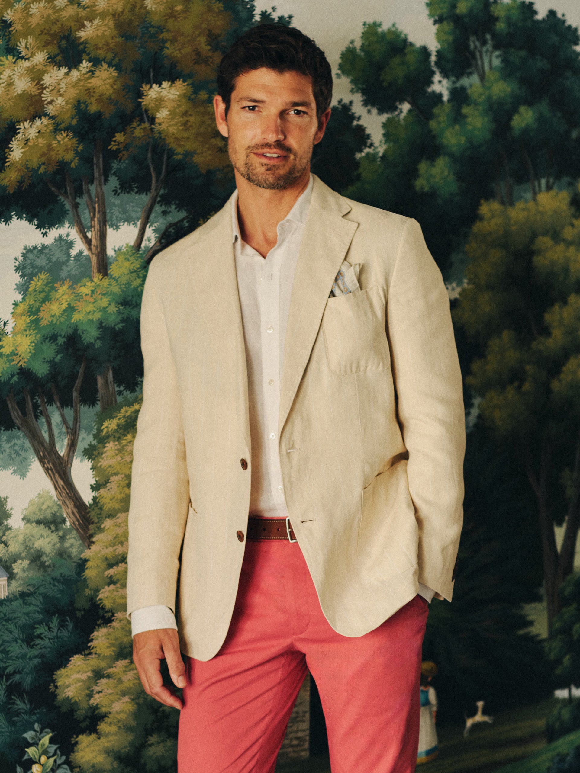 A man wearing a Brera Linen Sport Coat in Pinstripe by J.McLaughlin in a light beige color over a white shirt paired with coral pants, embodying effortlessly stylish, enduring designs with a legacy of timeless fashion. A destination for defining style. Life, Well-Lived.
