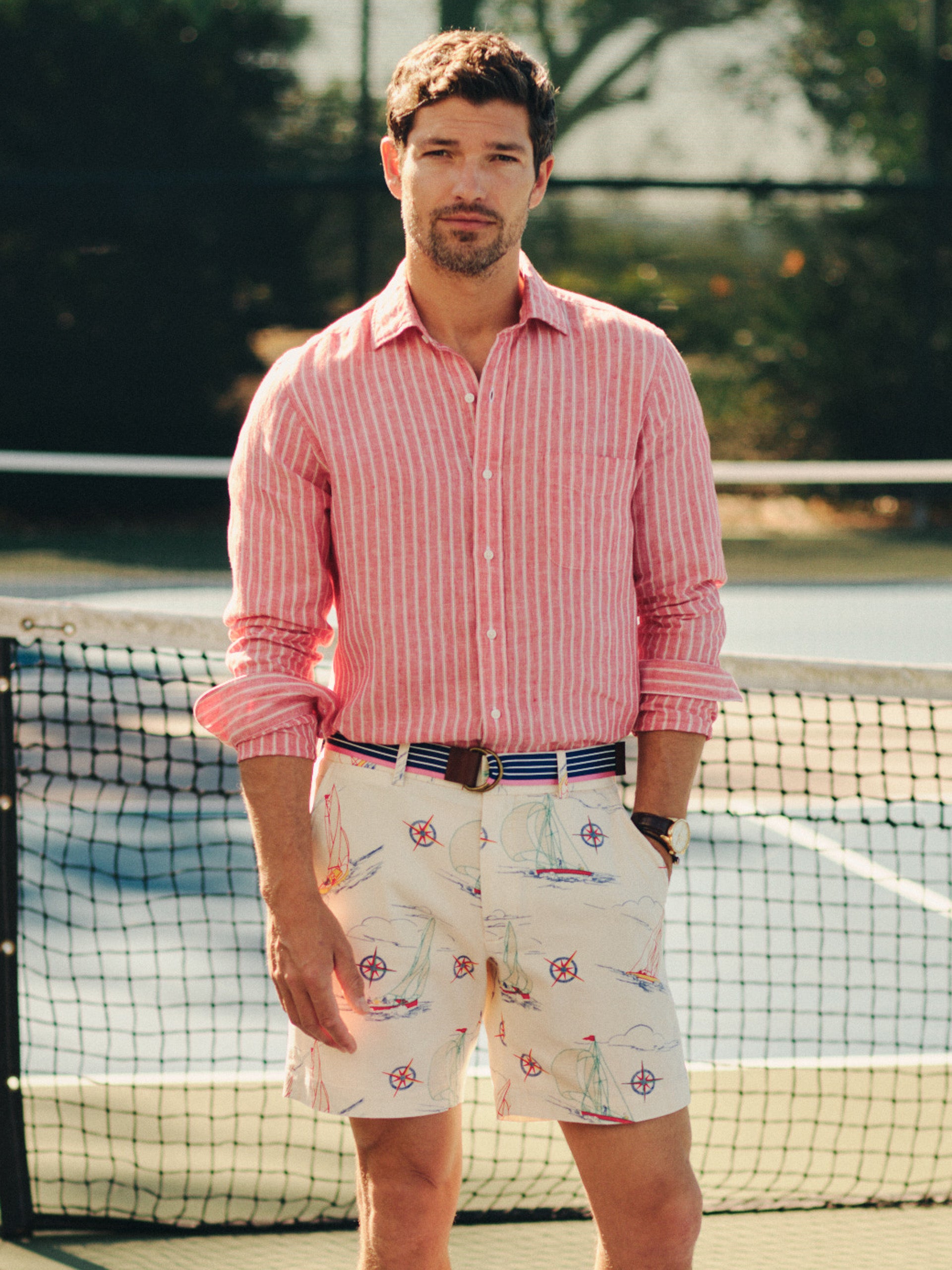 Man wearing J.McLaughlin Chatham Shorts in Compass Points featuring nautical designs paired with a casual red striped shirt and a belt, showcasing effortlessly stylish, enduring designs.