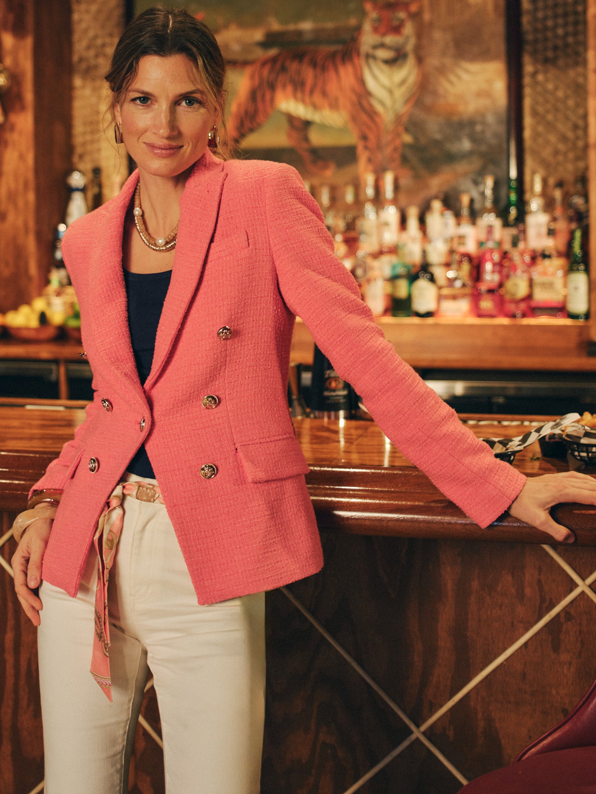 Woman wearing a vibrant pink Genevieve Cotton Bouclé Blazer by J.McLaughlin, paired with white pants and layered necklaces, embodying effortlessly stylish, enduring designs.