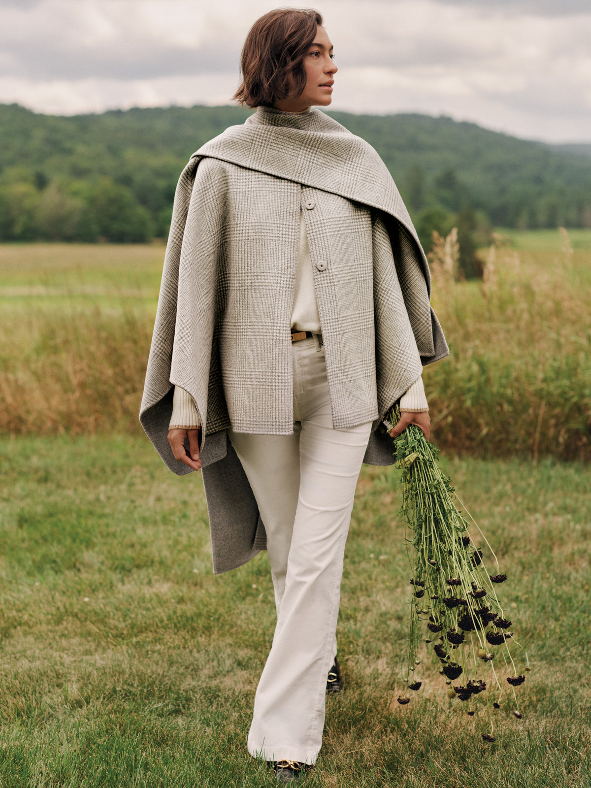 J.McLaughlin Haley Reversible Cape in Plaid styled on a woman outdoors with a softly draped scarf and classic neutral trousers