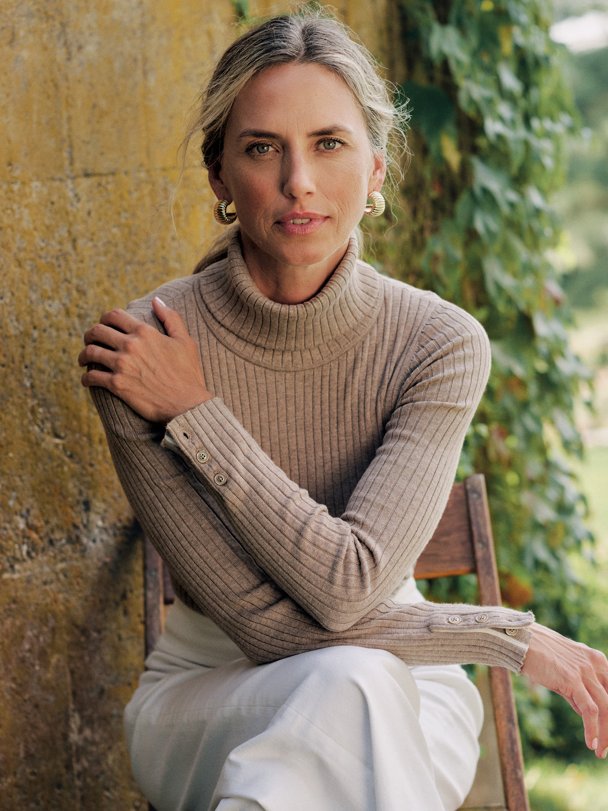 J.McLaughlin Arlette Turtleneck in finely ribbed taupe stretch cotton modal with button cuffs worn by a seated woman in timeless style