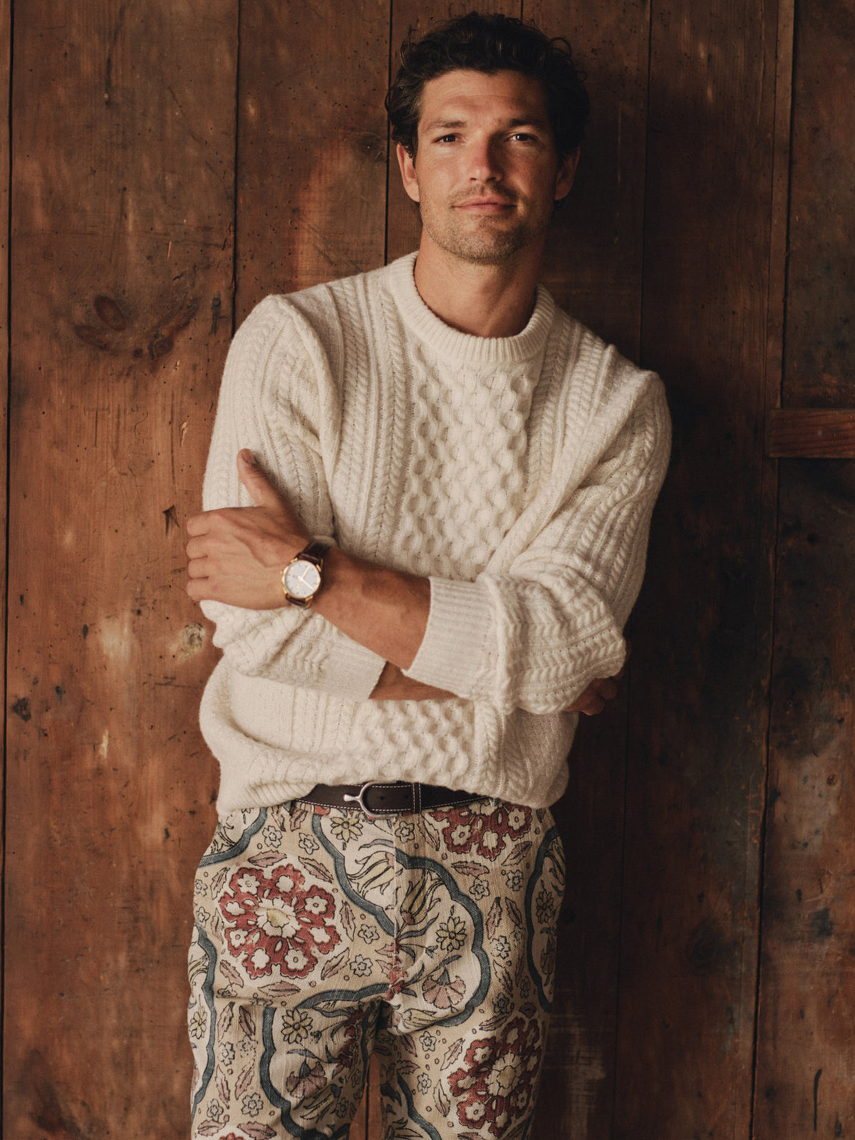 J.McLaughlin Aidan Sweater in a soft cream cable knit styled on a man with patterned pants against a warm wood wall