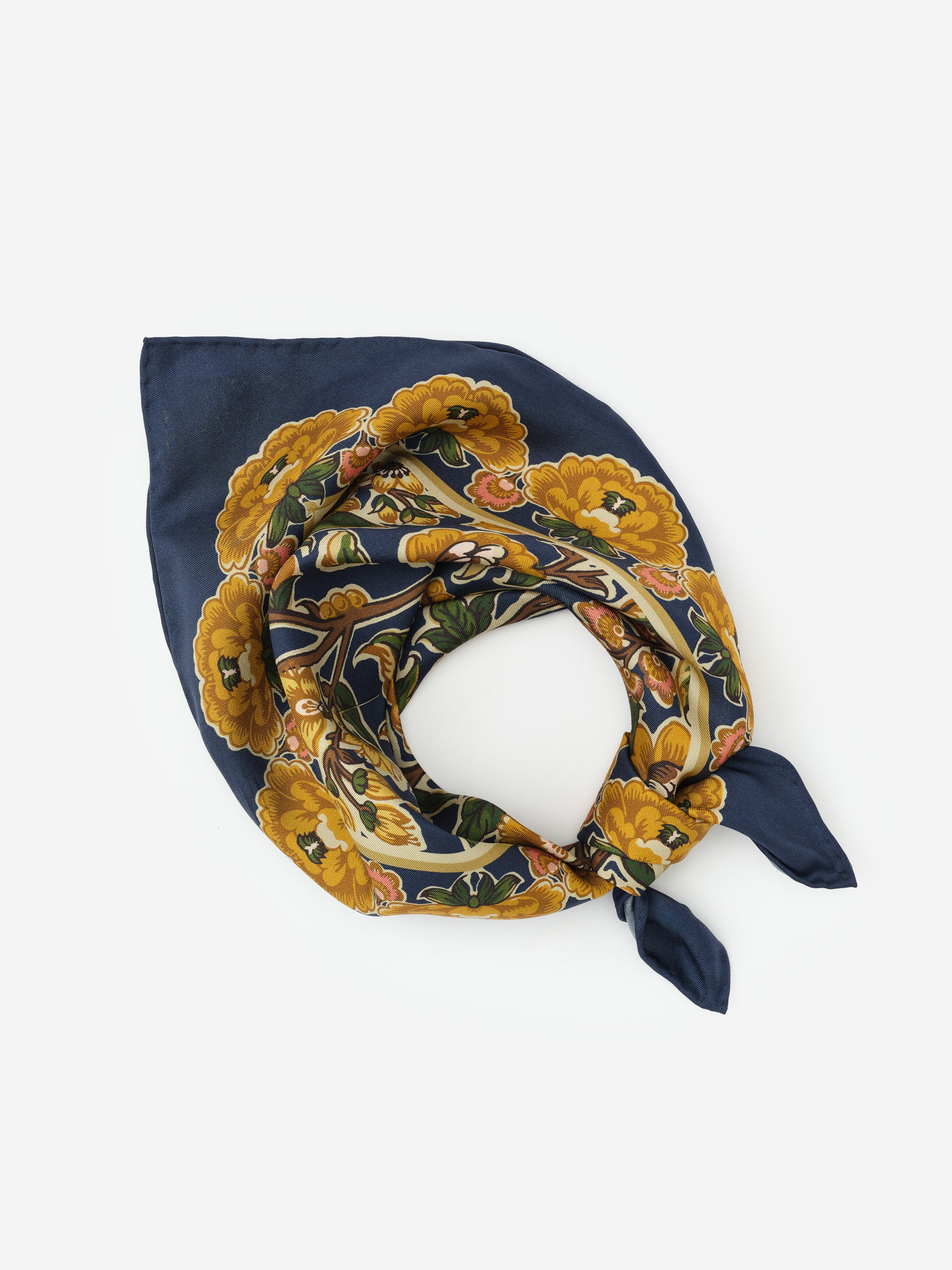 A folded Nikka Silk Scarf in Bucolic Blooms Kerchief featuring vibrant yellow floral patterns on a deep blue background, embodying J.McLaughlin’s legacy of timeless fashion with effortlessly stylish, enduring designs and innovative fabrics, a destination for defining style. Life, Well-Lived.