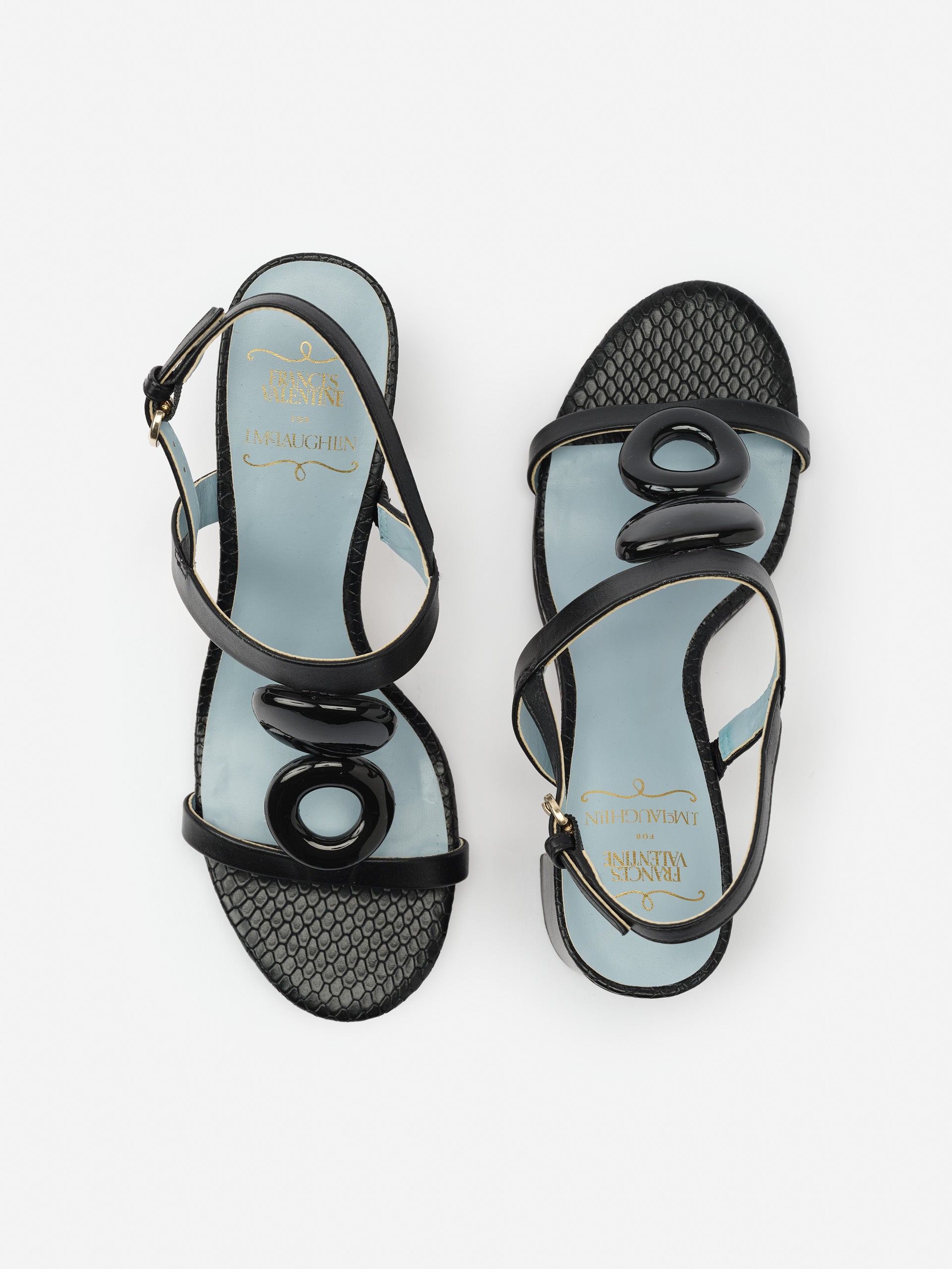 Bianca Heels by J.McLaughlin feature effortlessly stylish black leather sandals with unique glossy oval embellishments, showcasing enduring designs and a legacy of timeless fashion.