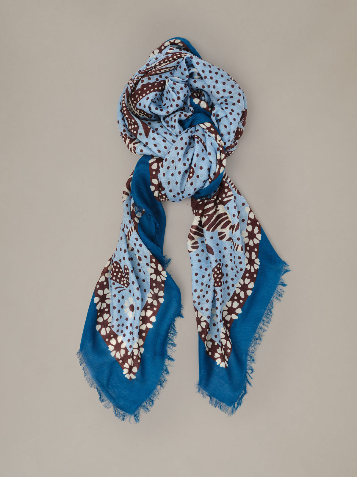 The Katherine Scarf in Folk Tale Border by J.McLaughlin shown as a blue and brown patterned scarf with fringed edges and a soft drape