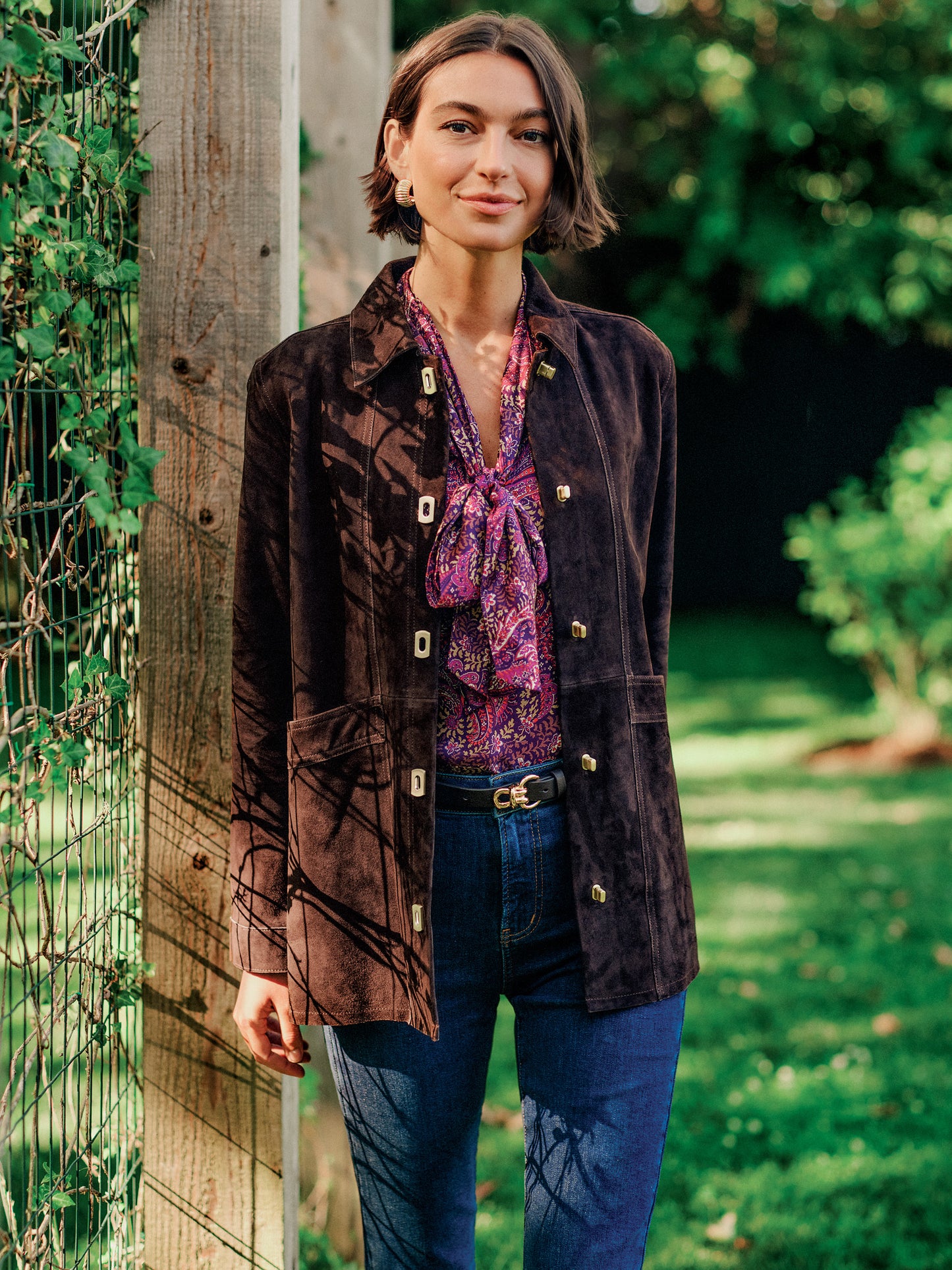 J.McLaughlin Kavya Suede Jacket in dark brown goat suede worn over a patterned blouse with jeans in a sunlit garden