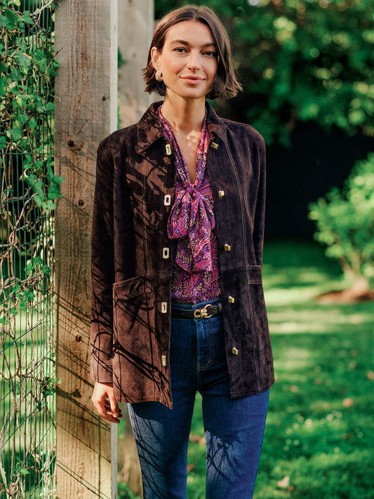 J.McLaughlin Kavya Suede Jacket in dark brown goat suede worn over a patterned blouse with jeans in a sunlit garden