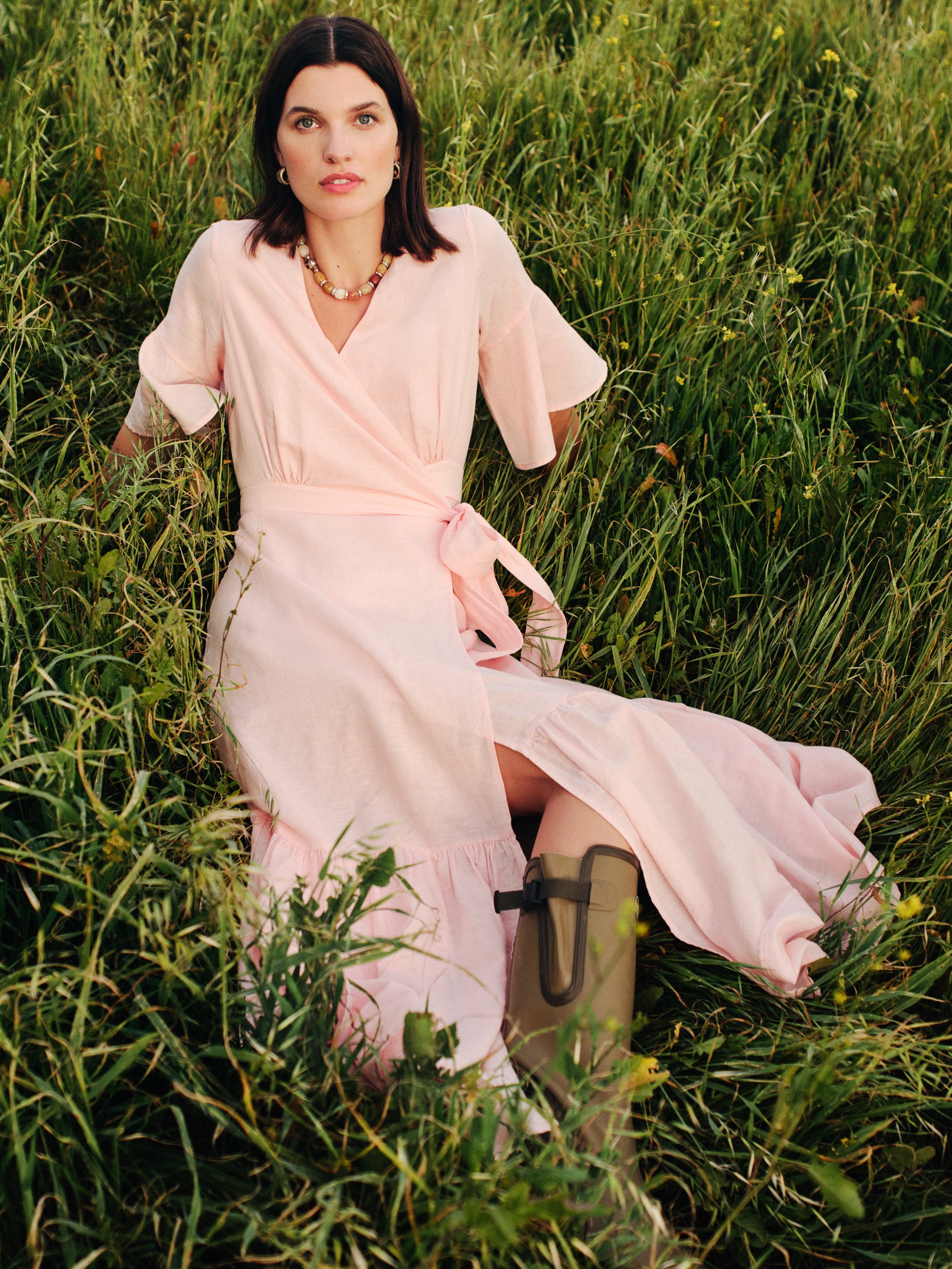 Woman sitting in a grassy field wearing the Emily Linen Blend Wrap Dress by J.McLaughlin, combining effortlessly stylish design with innovative fabrics for enduring appeal.