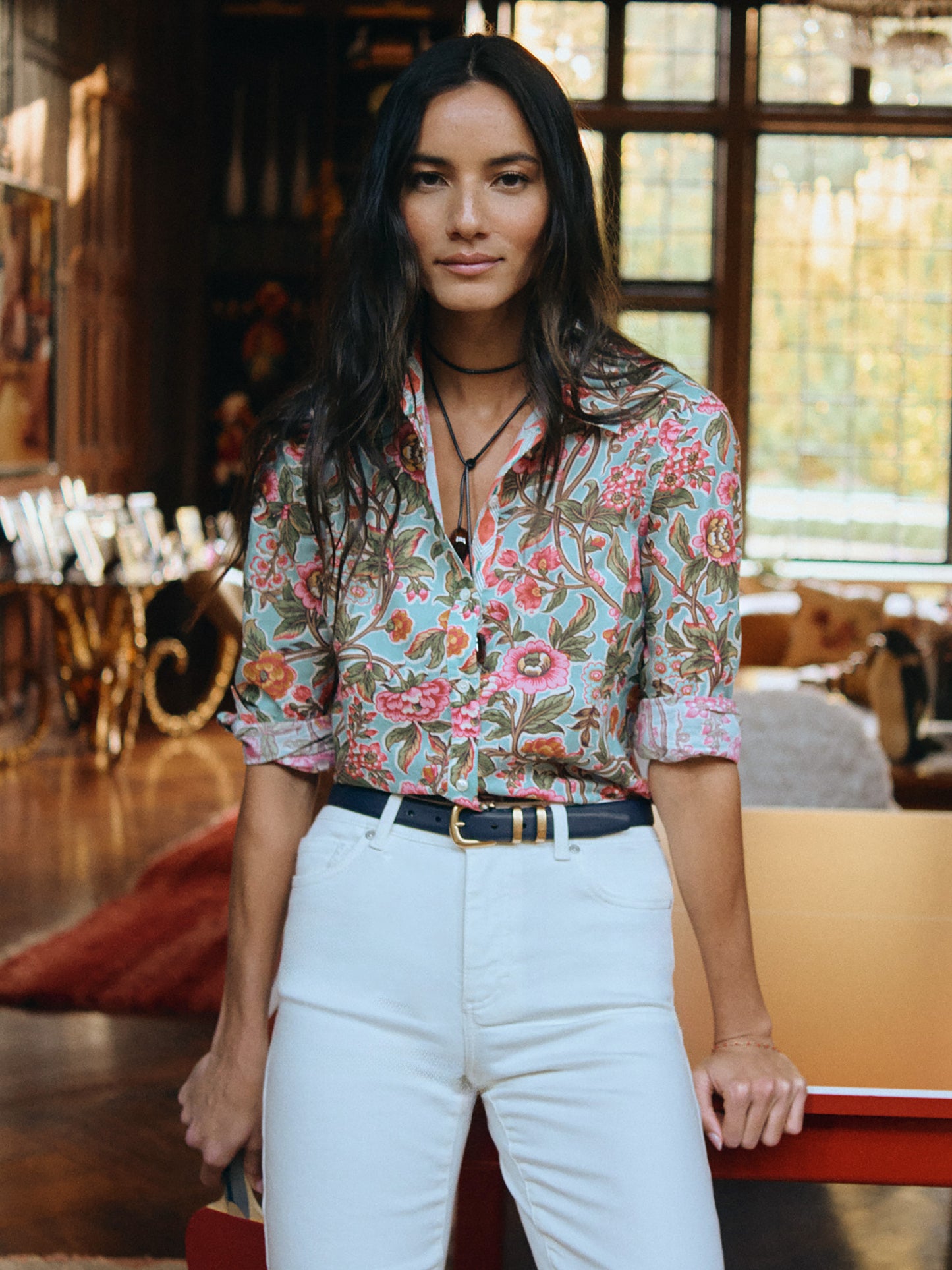 Woman wearing the Lois Shirt in Bucolic Beekeeper by J.McLaughlin, featuring a floral pattern shirt paired with white pants and a black belt, embodying effortlessly stylish, enduring designs.