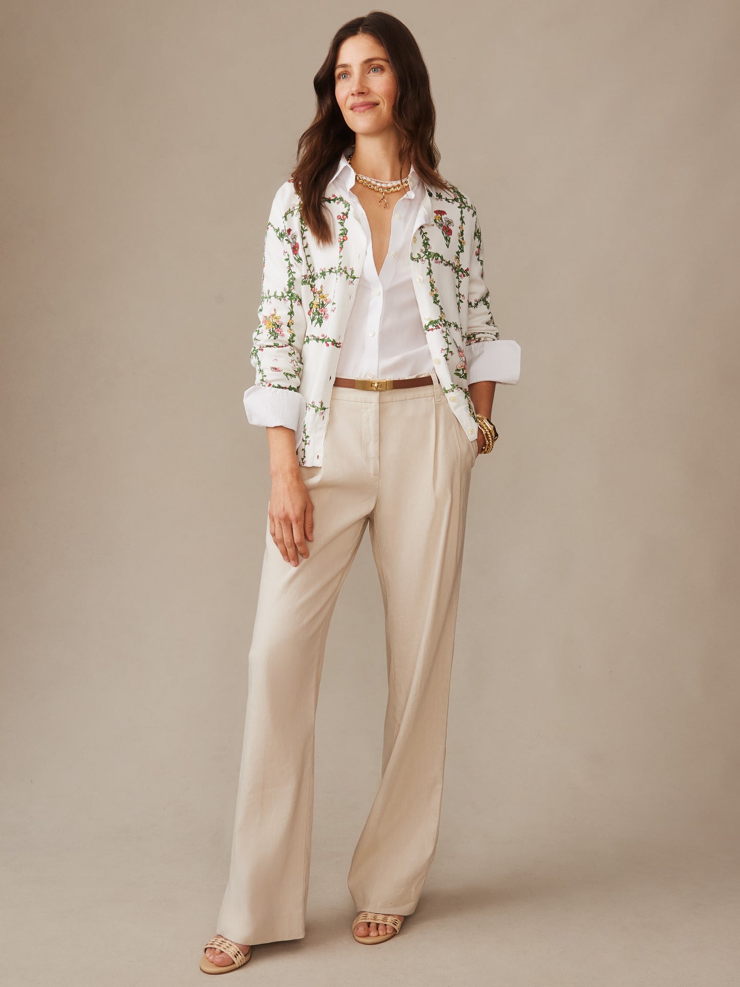 Woman wearing a Whitney Cardigan in Floral Medley Frame by J.McLaughlin, styled with a white shirt and beige pants, showcasing effortlessly stylish, enduring designs and a legacy of timeless fashion.