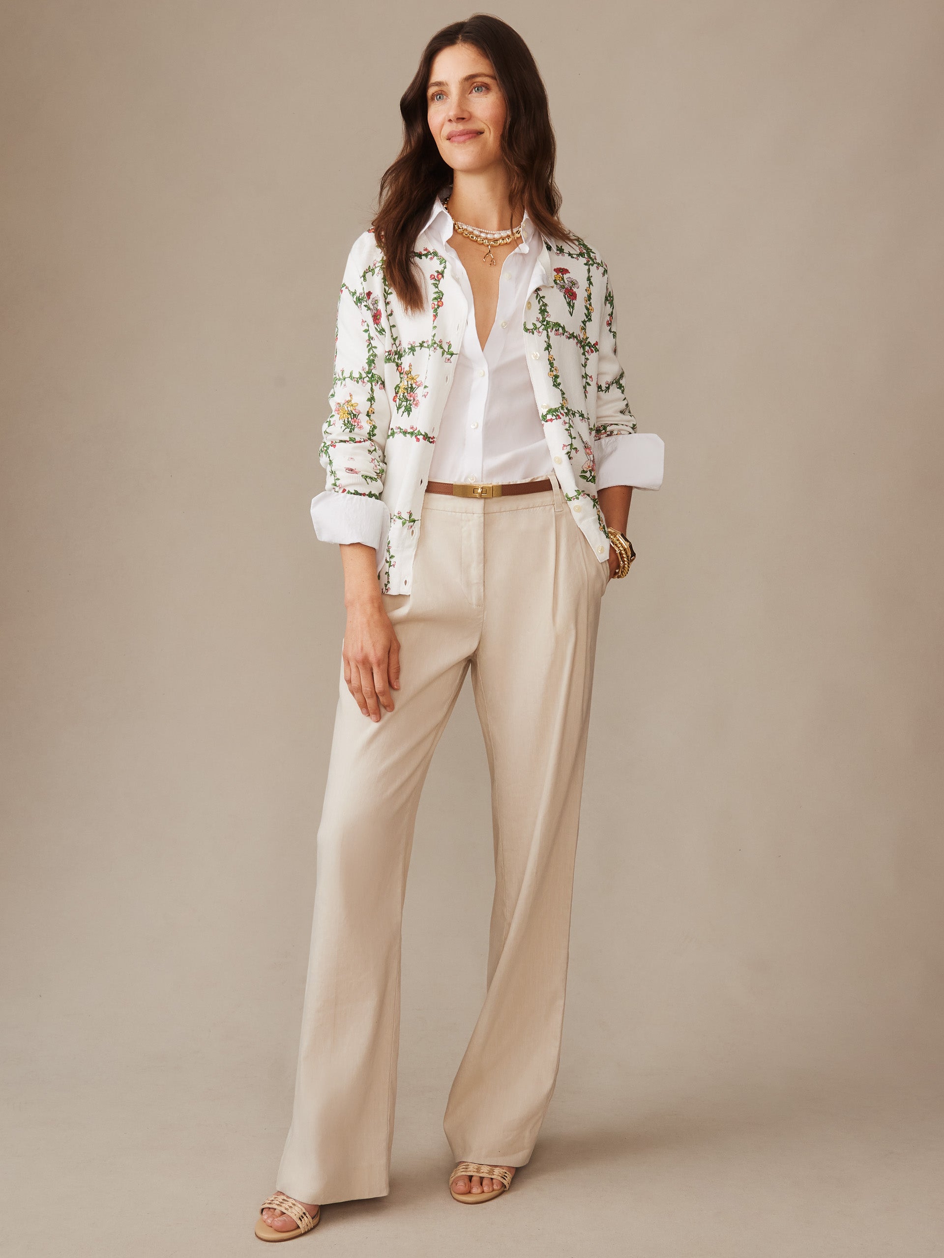 Woman wearing a Whitney Cardigan in Floral Medley Frame by J.McLaughlin, styled with a white shirt and beige pants, showcasing effortlessly stylish, enduring designs and a legacy of timeless fashion.
