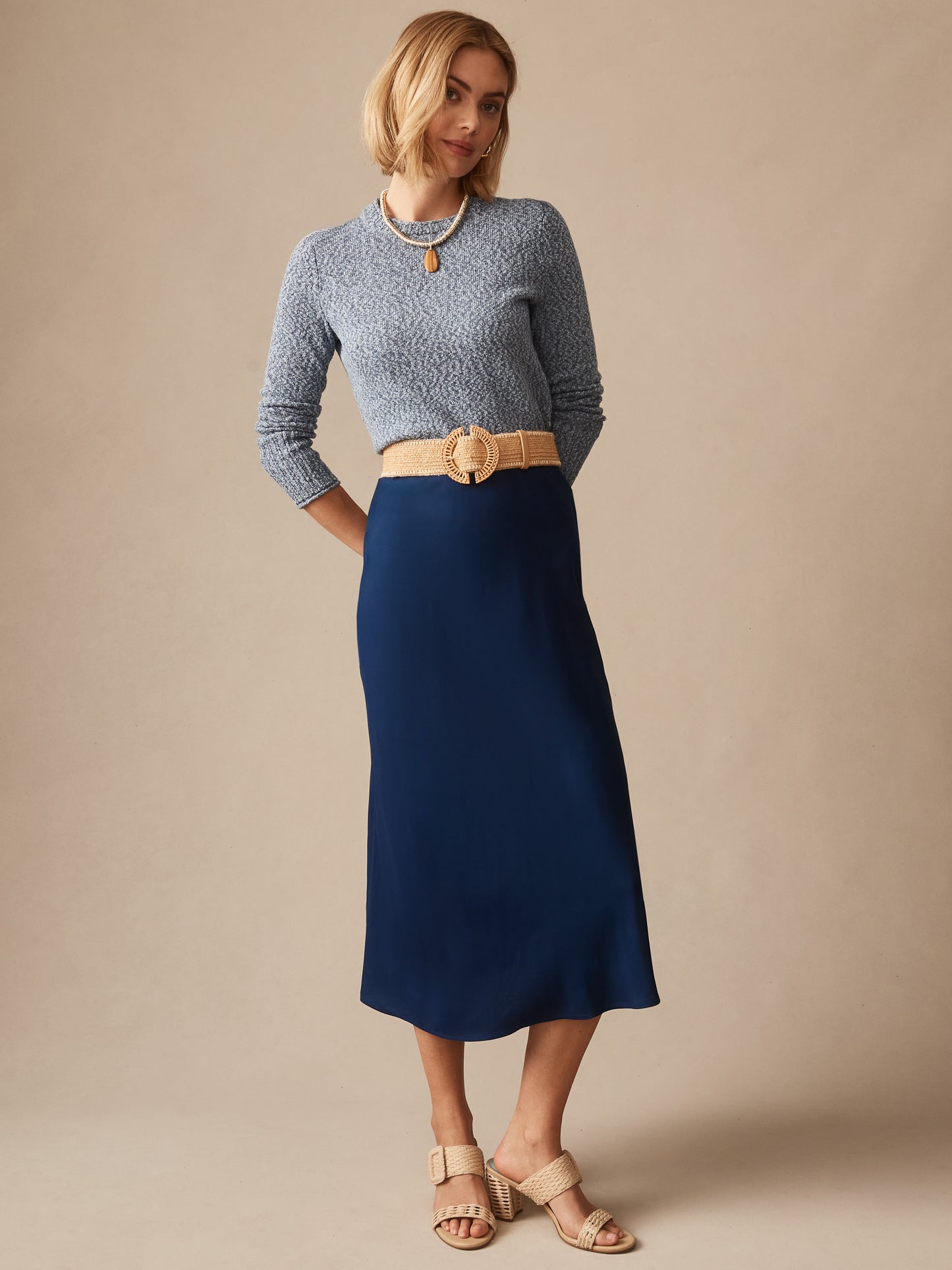 Woman wearing a navy Mae Sweater by J.McLaughlin, paired with a beige belt and matching sandals, showcasing effortlessly stylish, enduring designs and innovative fabrics.