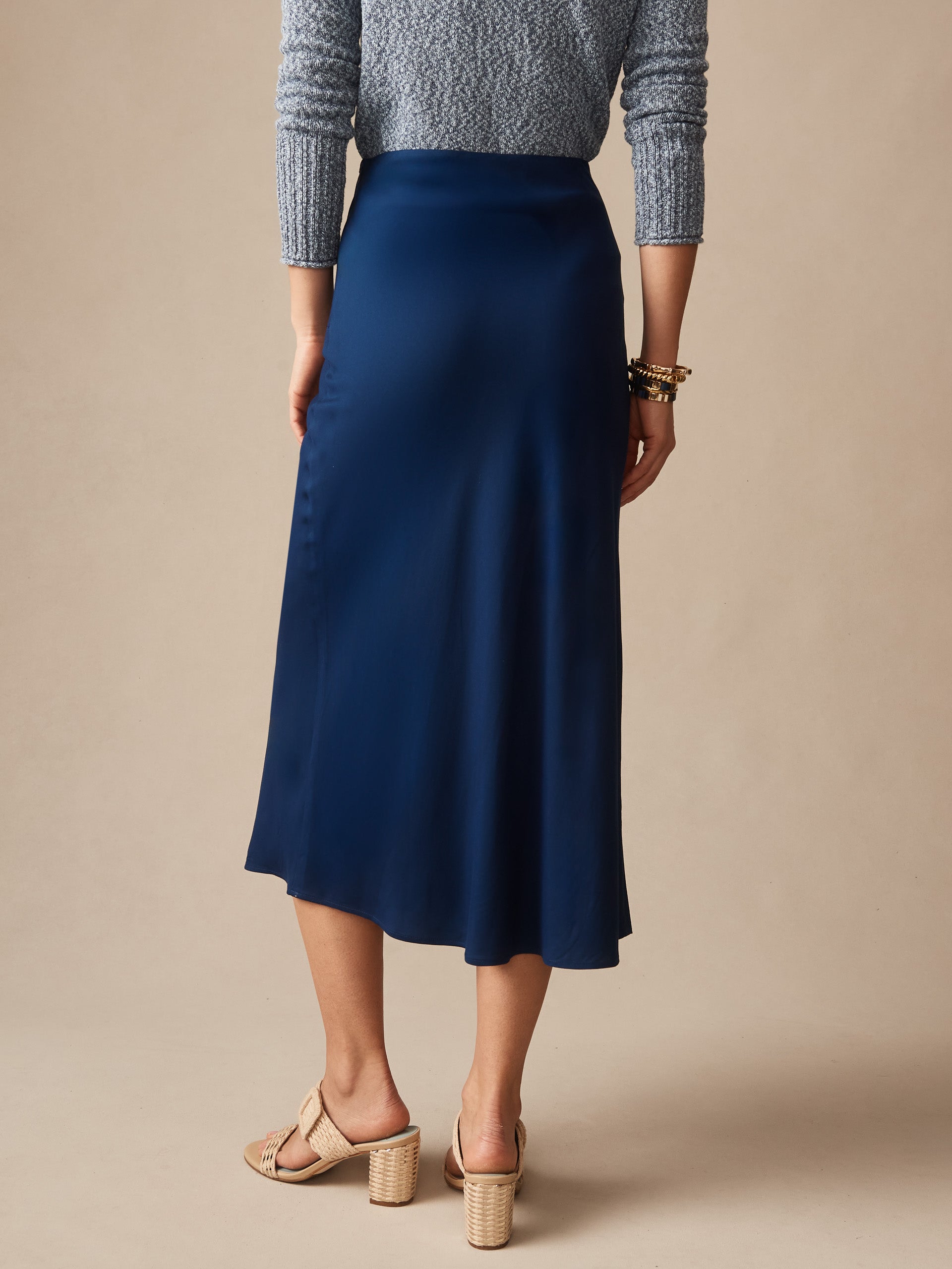 Back view of a woman wearing a navy Adelyn Skirt by J.McLaughlin paired with a textured gray top and beige heeled sandals, showcasing effortlessly stylish, enduring designs.