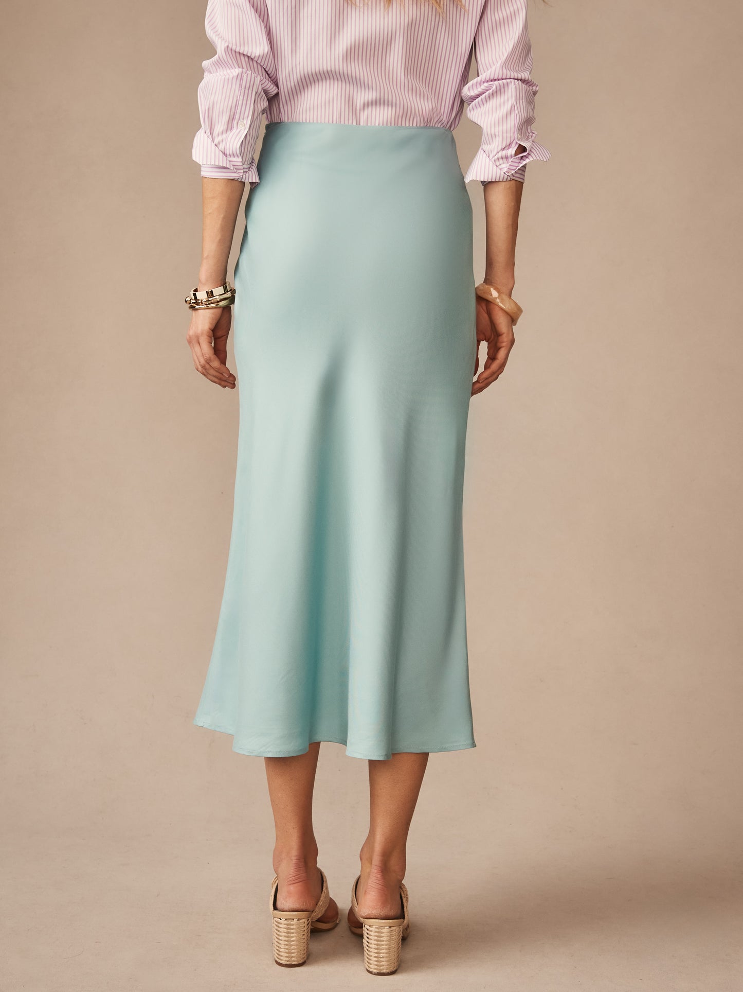 Woman wearing a soft blue Adelyn Skirt by J.McLaughlin, paired with a striped blouse and heels, showcasing effortlessly stylish, enduring designs and innovative fabrics.
