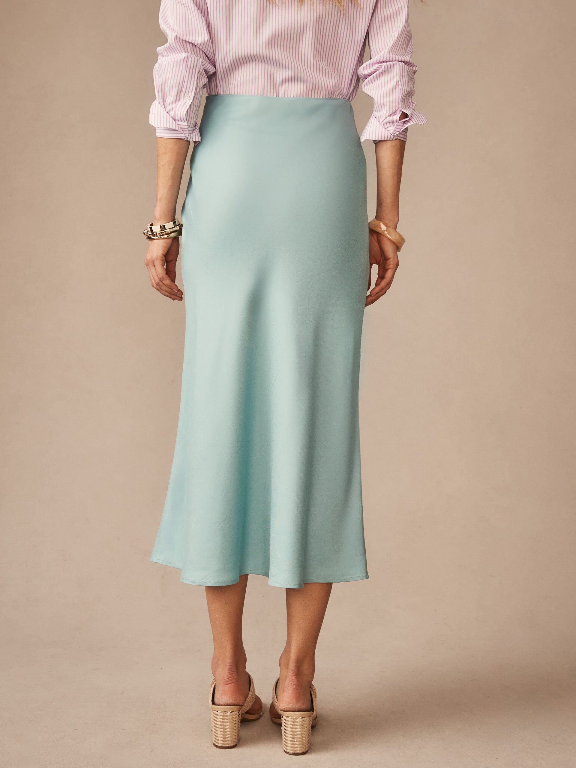 Woman wearing a soft blue Adelyn Skirt by J.McLaughlin, paired with a striped blouse and heels, showcasing effortlessly stylish, enduring designs and innovative fabrics.