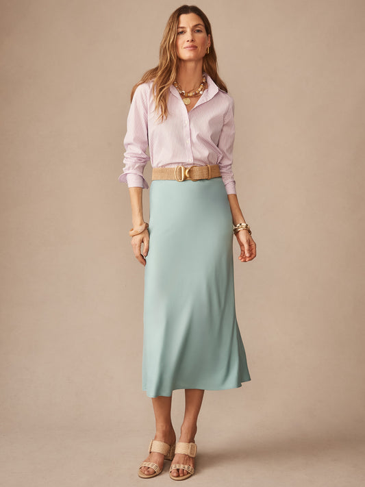 A confident woman wears the J.McLaughlin Adelyn Skirt in soft blue paired with a striped shirt and woven belt, showcasing effortlessly stylish, enduring designs crafted with innovative fabrics.