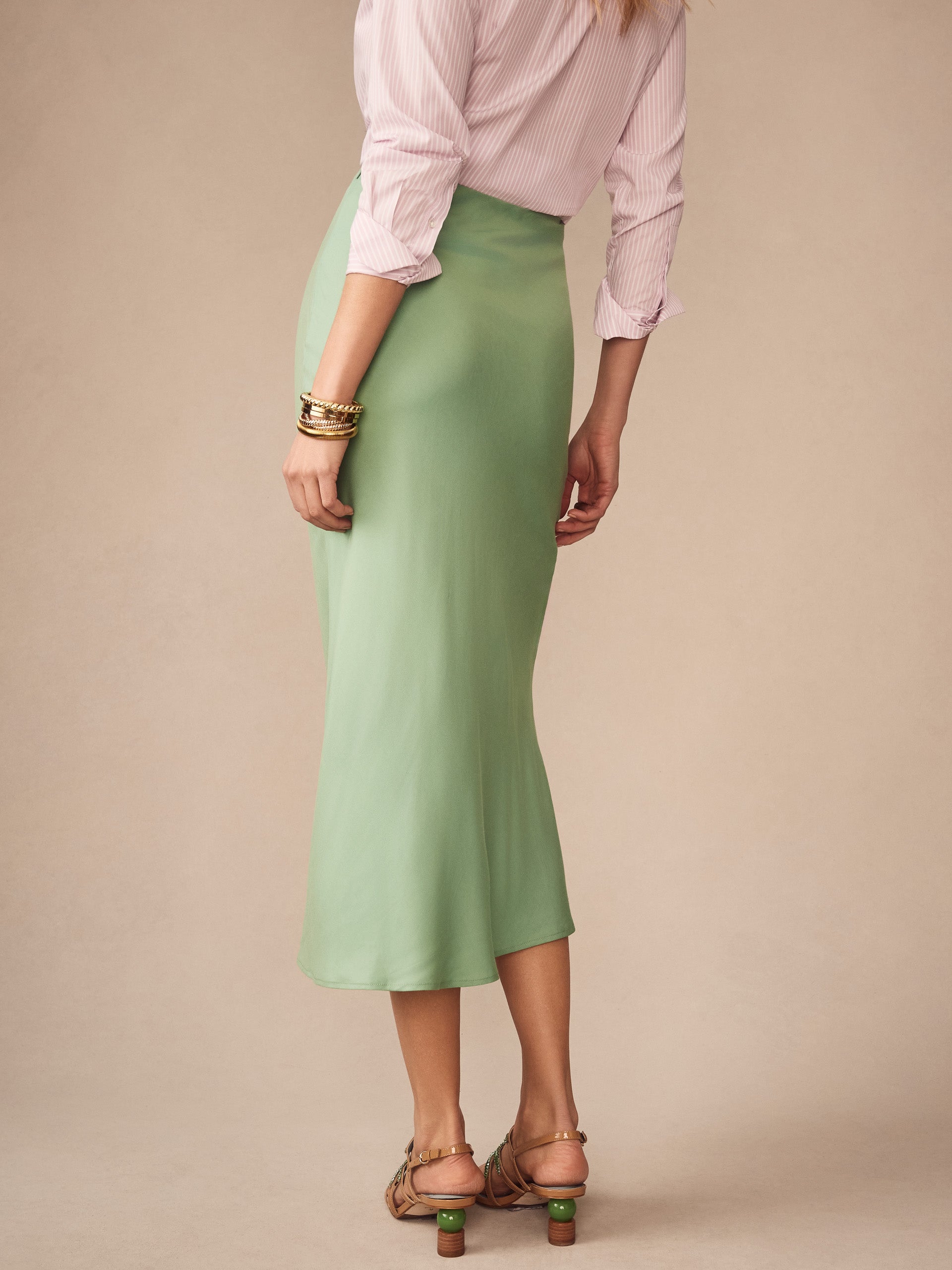 Woman wearing a soft green Adelyn Skirt by J.McLaughlin paired with a light pink blouse and sandals, showcasing effortlessly stylish, enduring designs with innovative fabrics.