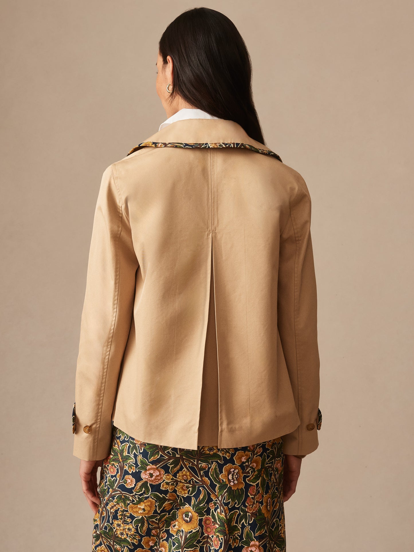 A woman wearing the Audrey Jacket by J.McLaughlin in khaki, paired with a floral skirt, showcasing effortlessly stylish and enduring designs that embody a legacy of timeless fashion.