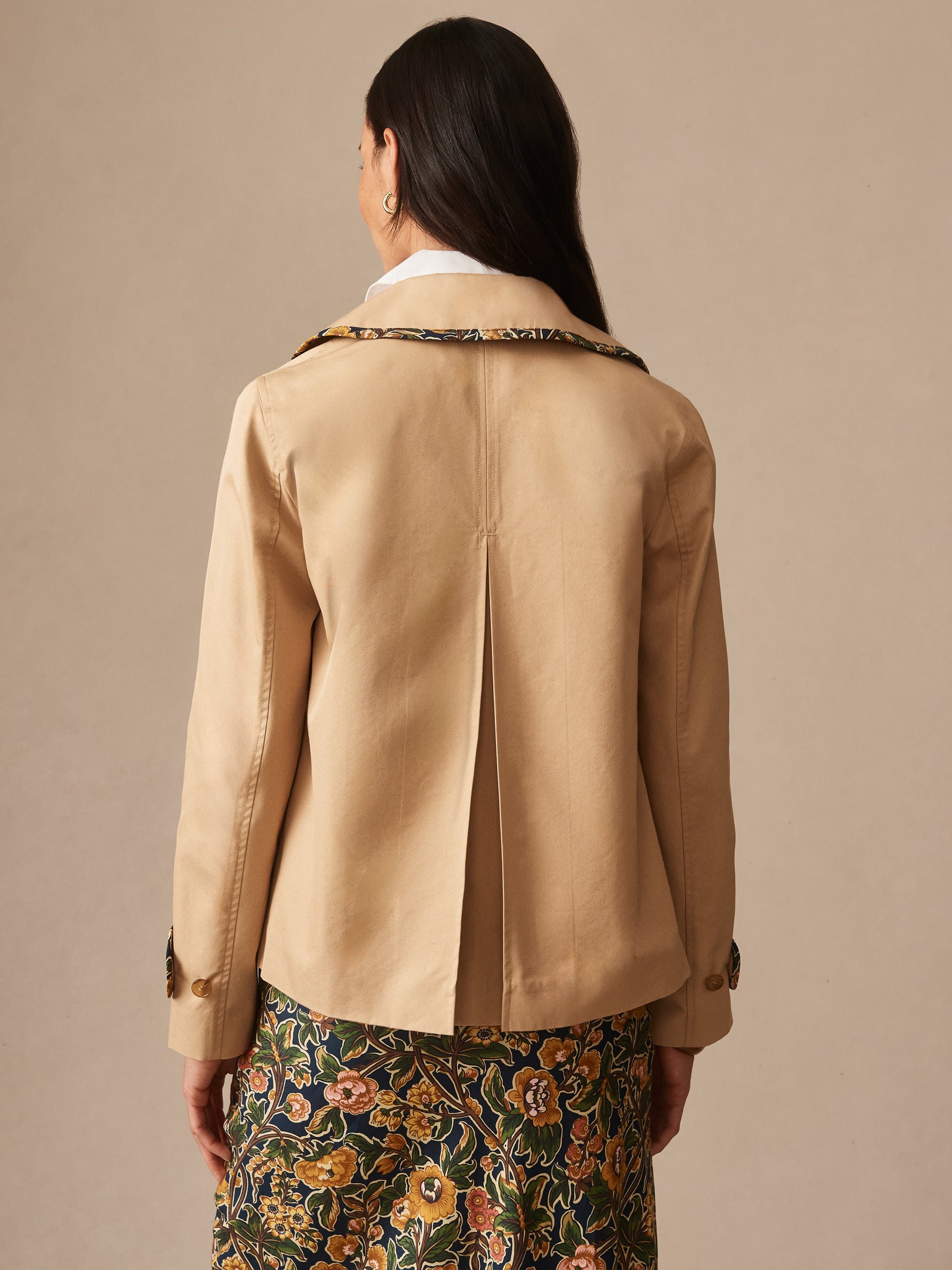 A woman wearing the Audrey Jacket by J.McLaughlin in khaki, paired with a floral skirt, showcasing effortlessly stylish and enduring designs that embody a legacy of timeless fashion.