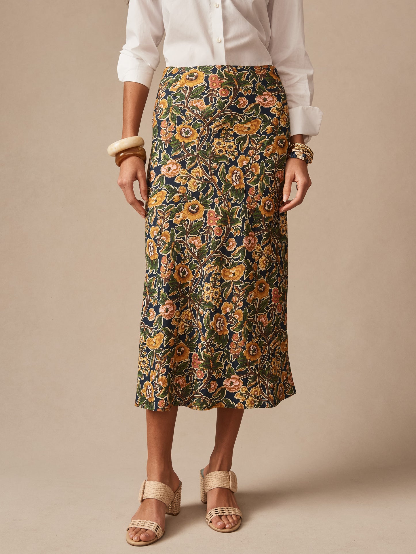 A model wears the Adelyn Skirt in Bucolic Blooms Bias by J.McLaughlin, featuring an effortlessly stylish floral print skirt paired with neutral sandals and a white blouse, showcasing enduring designs and innovative fabrics from a destination for defining style. Life, Well-Lived.