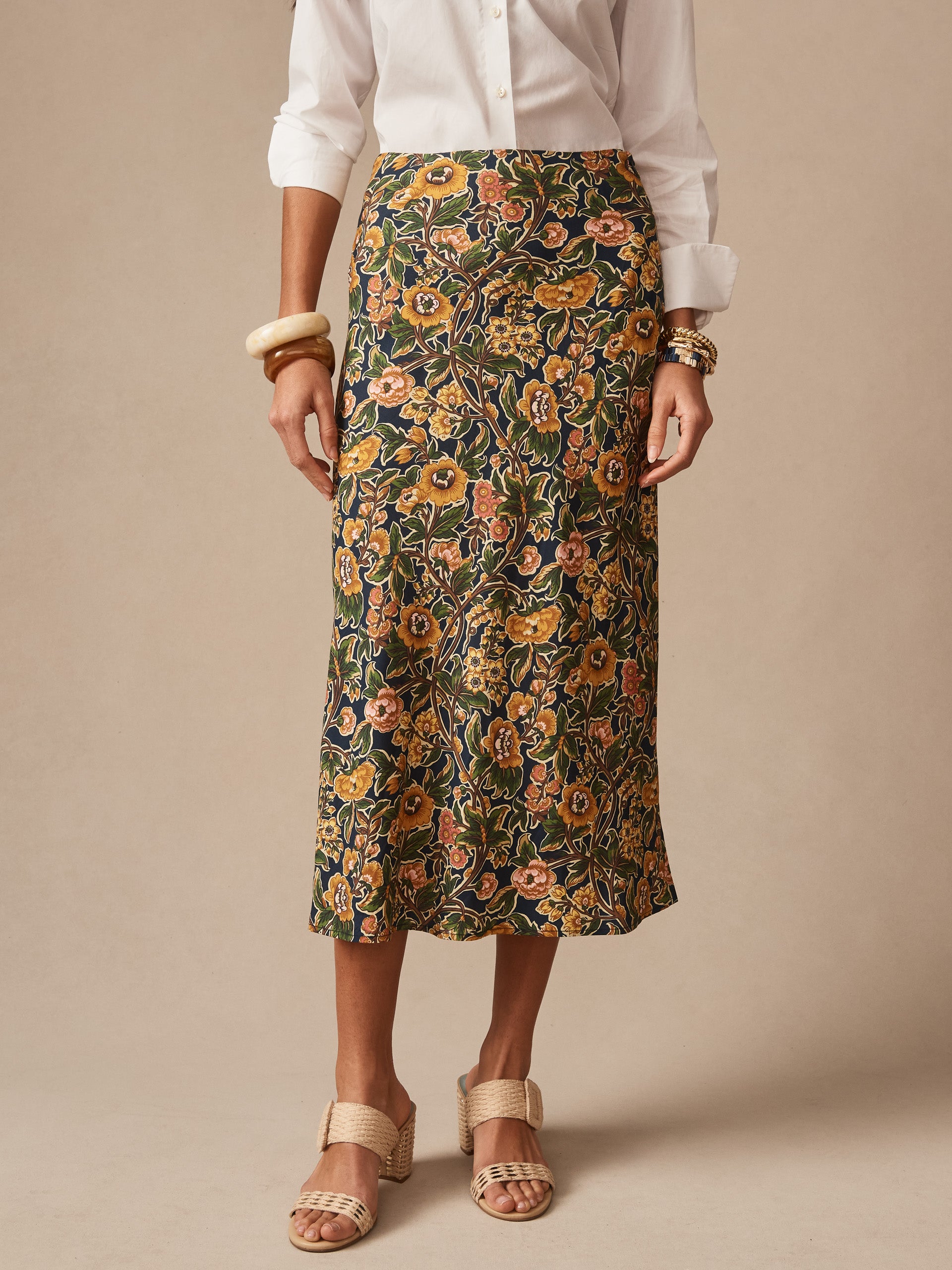 A model wears the Adelyn Skirt in Bucolic Blooms Bias by J.McLaughlin, featuring an effortlessly stylish floral print skirt paired with neutral sandals and a white blouse, showcasing enduring designs and innovative fabrics from a destination for defining style. Life, Well-Lived.