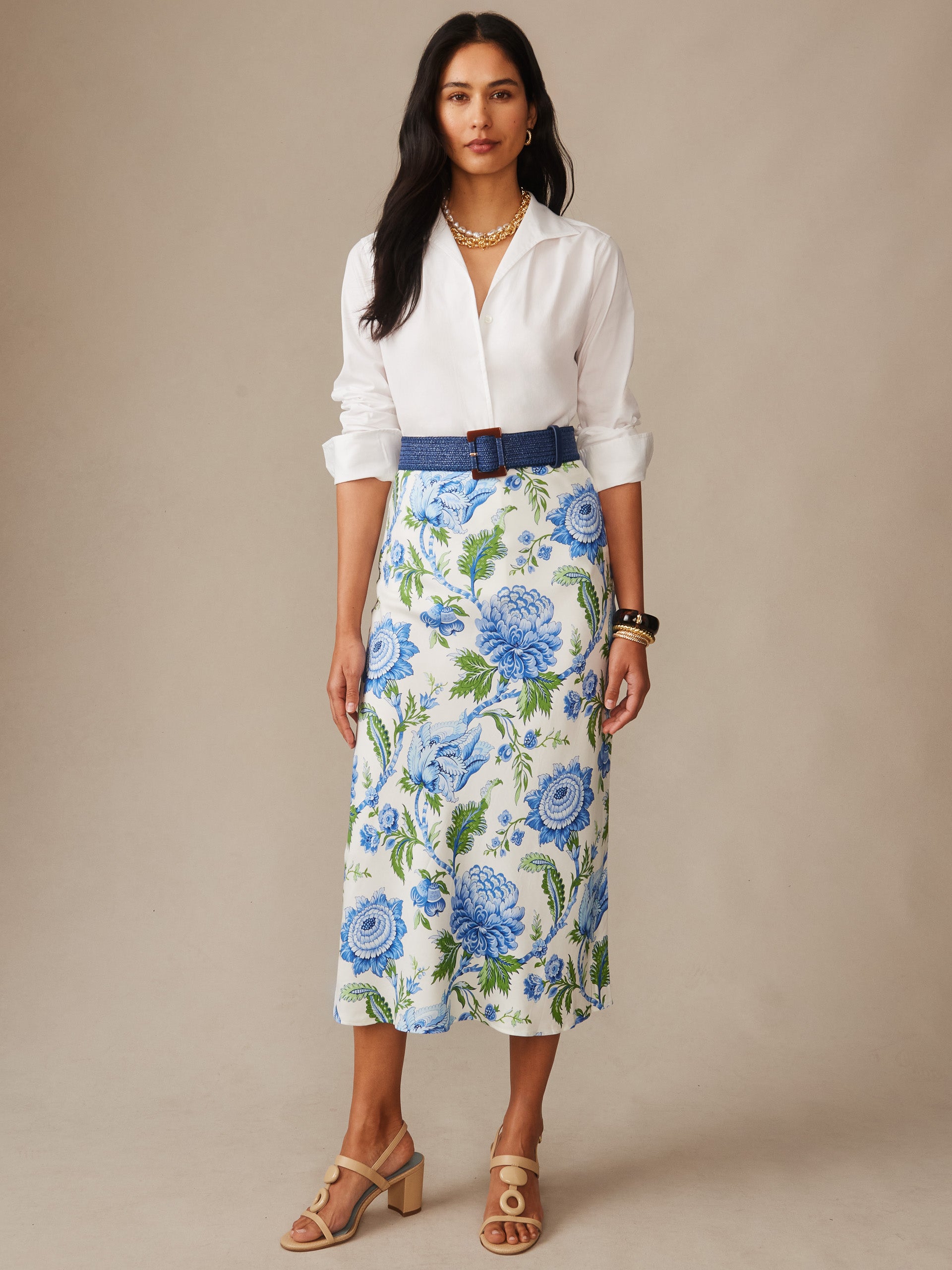 A woman wearing the Adelyn Silk Blend Skirt in Cerulean Garden Bias by J.McLaughlin paired with a white blouse, styled with a blue belt and sandals, showcasing effortlessly stylish, enduring designs and innovative fabrics in a legacy of timeless fashion. A destination for defining style. Life, Well-Lived.