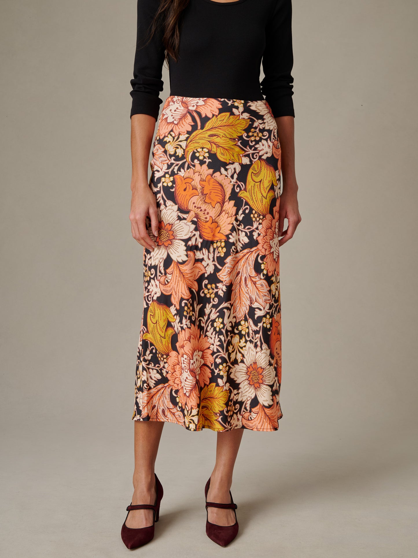 Woman wearing Adelyn Silk Blend Skirt in City Garden Bias by J.McLaughlin featuring a flowing floral pattern with warm autumn tones, styled with a black top and burgundy heels.