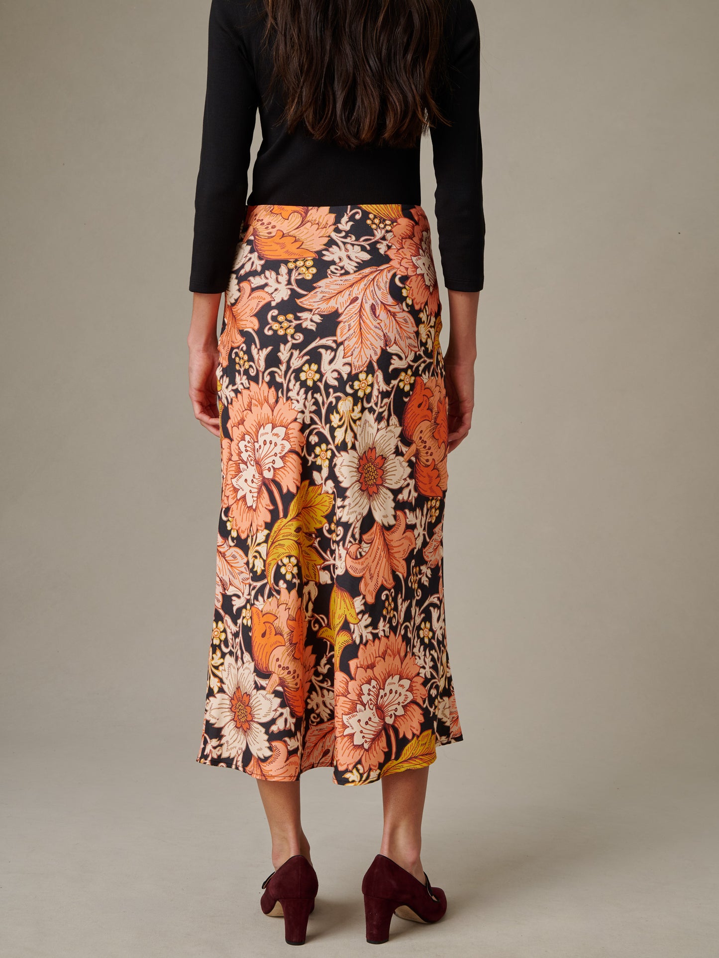 Woman wearing a floral patterned Adelyn Silk Blend Skirt in City Garden Bias by J.McLaughlin, paired with a black top and burgundy heels, showcasing timeless style and craftsmanship.