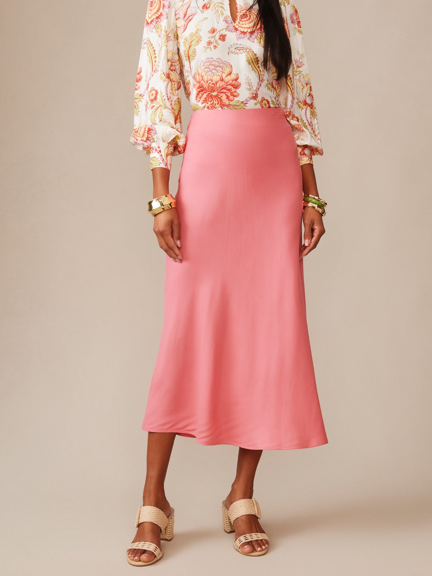 Model wearing a soft coral Adelyn Silk Blend Skirt by J.McLaughlin paired with a patterned blouse and woven sandals, showcasing effortlessly stylish, enduring designs.