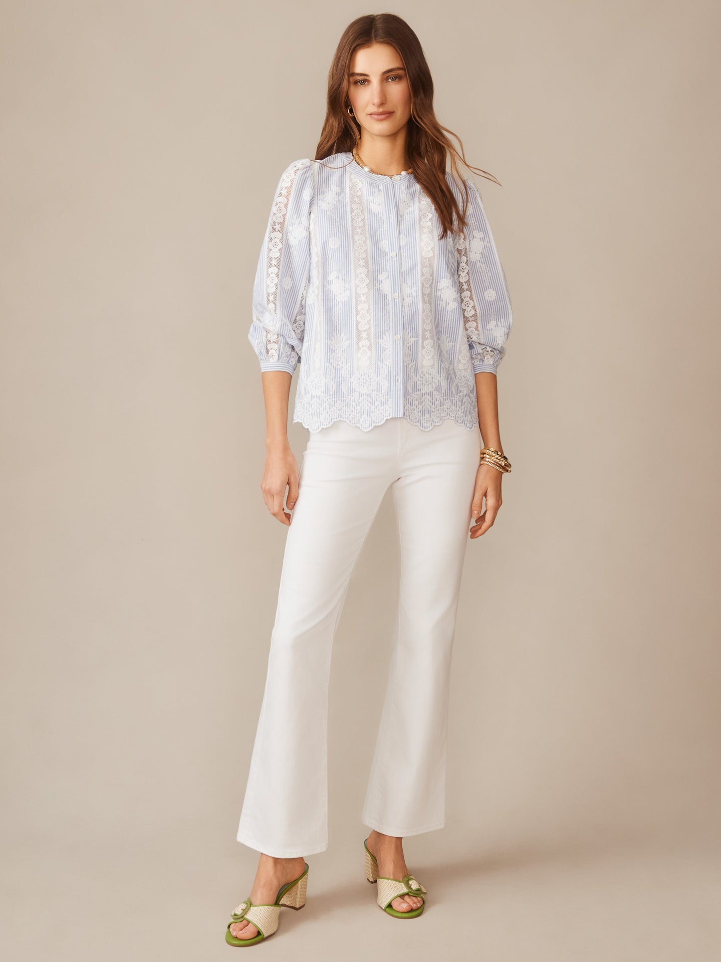 Woman wearing the Alice Blouse in Stripe by J.McLaughlin, featuring delicate lace details and a soft blue and white striped pattern, paired with white pants and green sandals, showcasing effortlessly stylish, enduring designs and innovative fabrics for a legacy of timeless fashion. A destination for defining style. Life, Well-Lived.