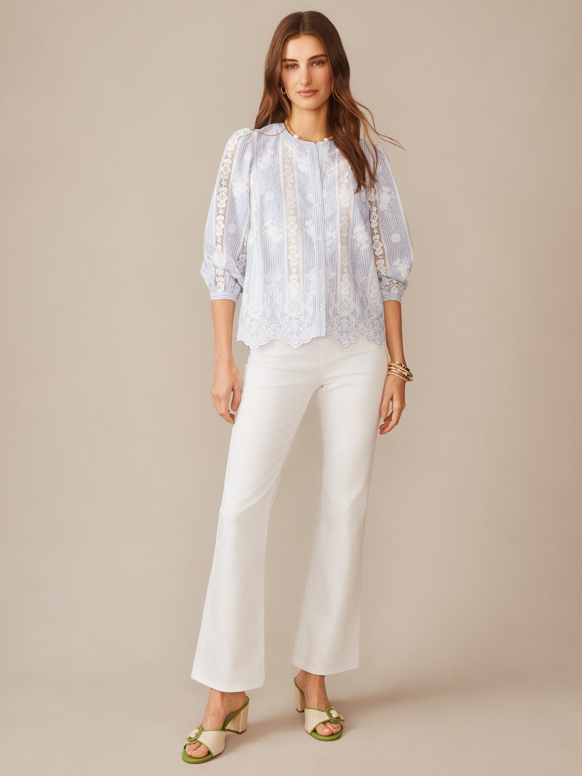 Woman wearing the Alice Blouse in Stripe by J.McLaughlin, featuring delicate lace details and a soft blue and white striped pattern, paired with white pants and green sandals, showcasing effortlessly stylish, enduring designs and innovative fabrics for a legacy of timeless fashion. A destination for defining style. Life, Well-Lived.