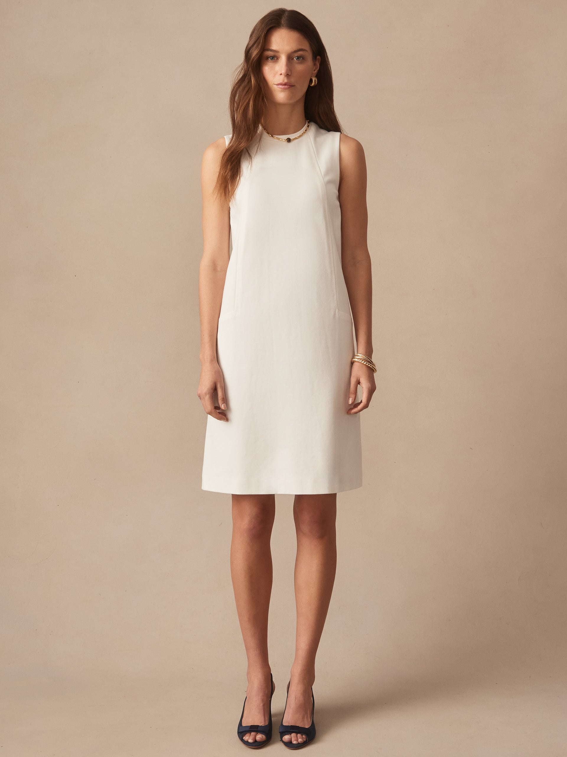 Woman wearing an ivory Alicia Dress by J.McLaughlin, featuring a sleeveless, classic silhouette pairing enduring designs with innovative fabrics for a legacy of timeless fashion.