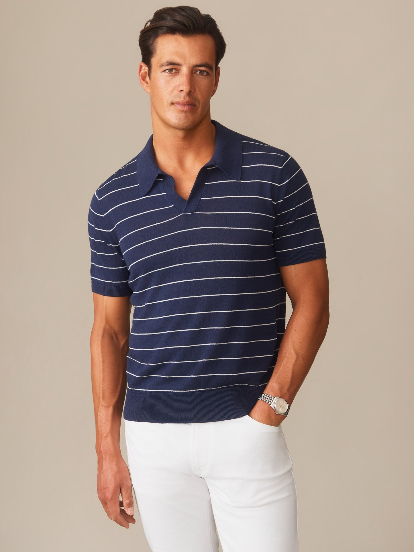 Man wearing a navy and white striped Amalfi Linen Blend Polo in Stripe by J.McLaughlin paired with white pants, showcasing effortlessly stylish, enduring designs with innovative fabrics.