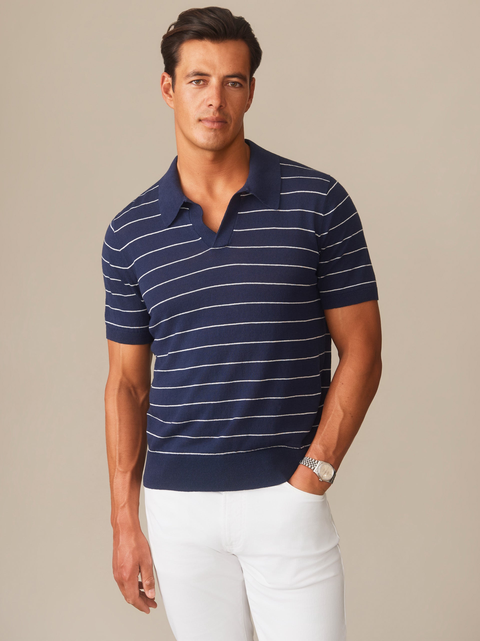 Man wearing a navy and white striped Amalfi Linen Blend Polo in Stripe by J.McLaughlin paired with white pants, showcasing effortlessly stylish, enduring designs with innovative fabrics.
