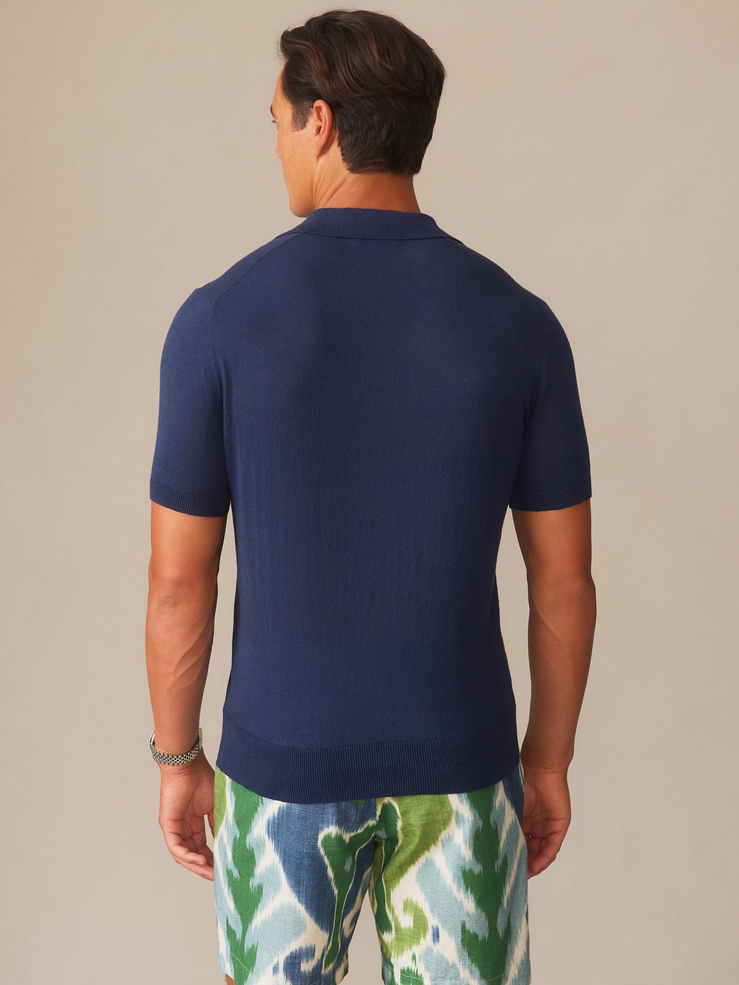 Man wearing a navy Amalfi Linen Blend Polo by J.McLaughlin, paired with patterned green and blue shorts, showcasing effortlessly stylish, enduring designs in innovative fabrics.