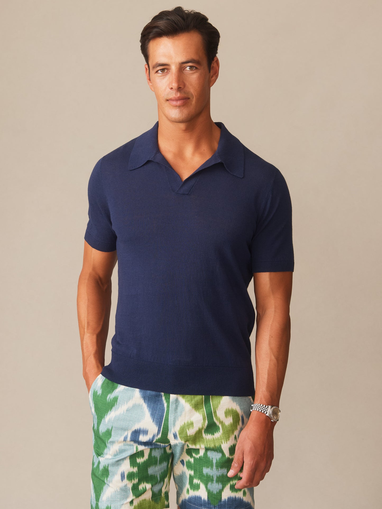 Man wearing a navy Amalfi Linen Blend Polo by J.McLaughlin paired with patterned green and blue shorts, showcasing effortlessly stylish, enduring designs in innovative fabrics.