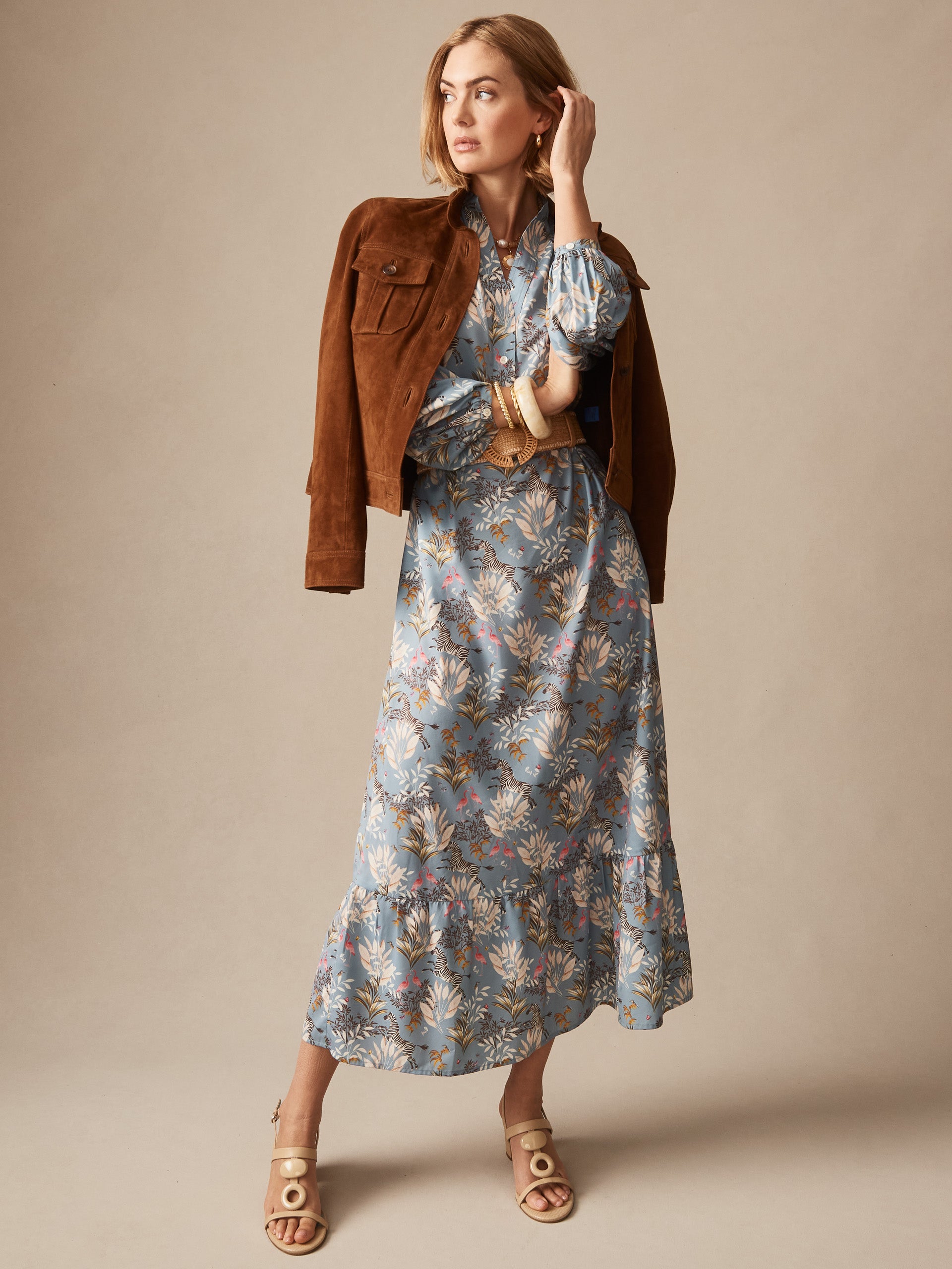 Woman wearing Amrita Dress in Zebra Story by J.McLaughlin, styled with a brown jacket and beige sandals, showcasing effortlessly stylish, enduring designs and a legacy of timeless fashion.