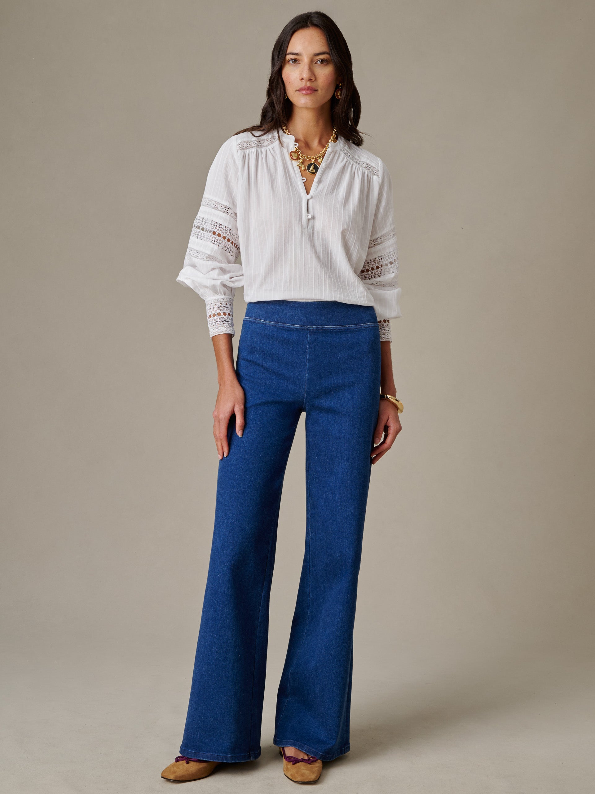 Woman modeling Anderson Jeans by J.McLaughlin, paired with a white blouse and gold jewelry, showcasing effortlessly stylish and enduring designs in classic blue denim.