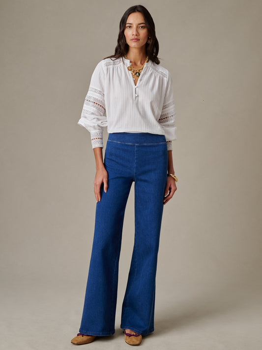 Woman modeling Anderson Jeans by J.McLaughlin, paired with a white blouse and gold jewelry, showcasing effortlessly stylish and enduring designs in classic blue denim.
