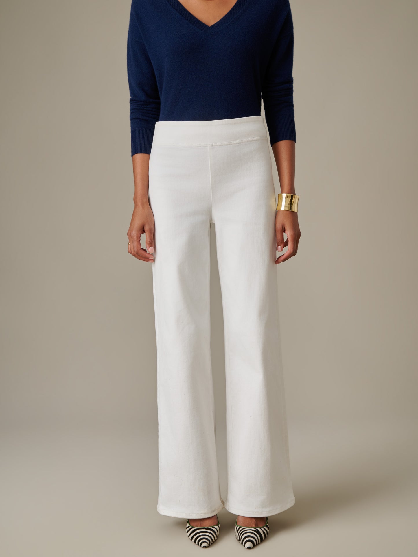 A stylish model wearing white Anderson Jeans paired with a navy blue top and statement gold cuff, showcasing J.McLaughlin's timeless craftsmanship and enduring design.