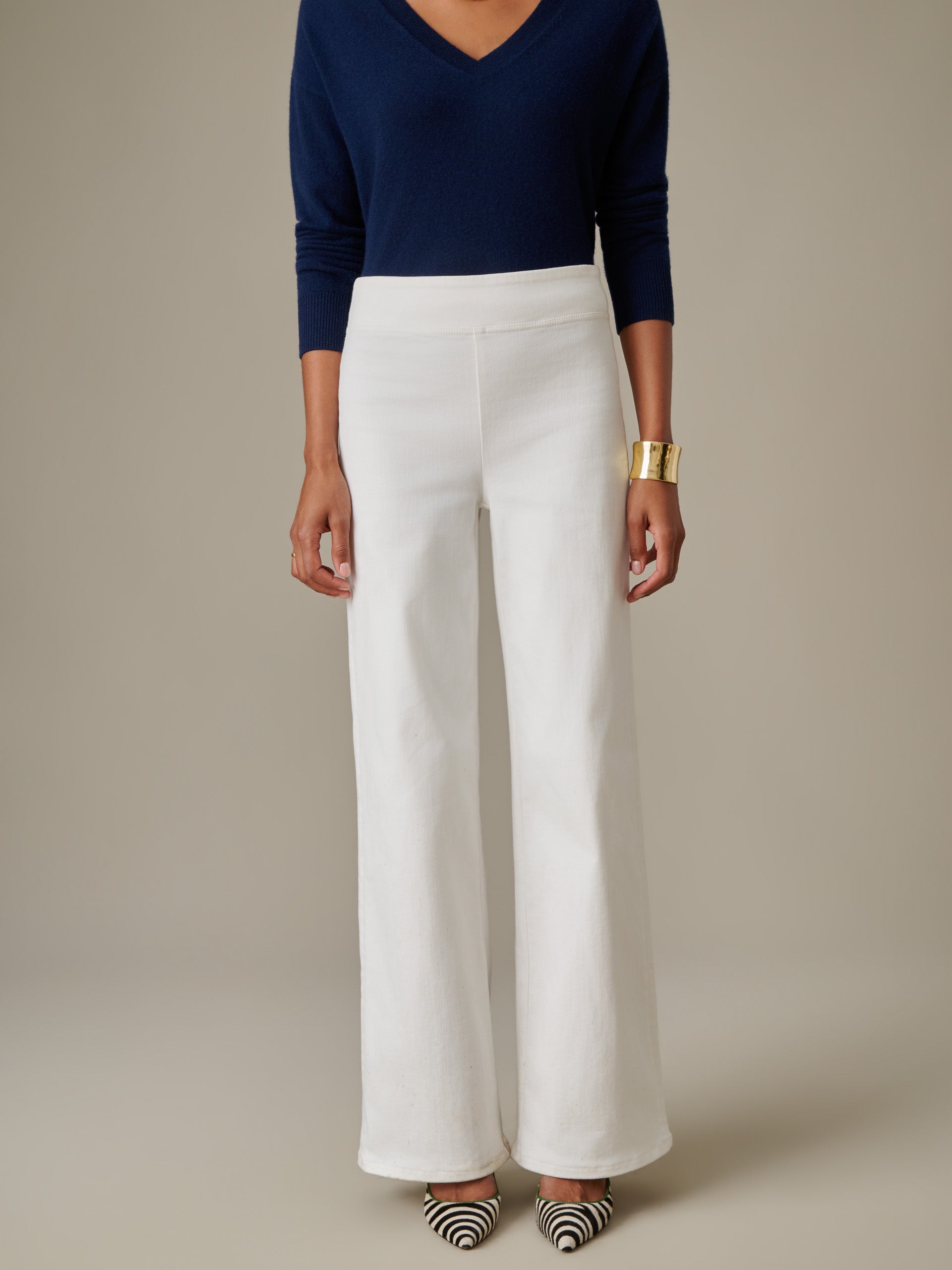 A stylish model wearing white Anderson Jeans paired with a navy blue top and statement gold cuff, showcasing J.McLaughlin's timeless craftsmanship and enduring design.