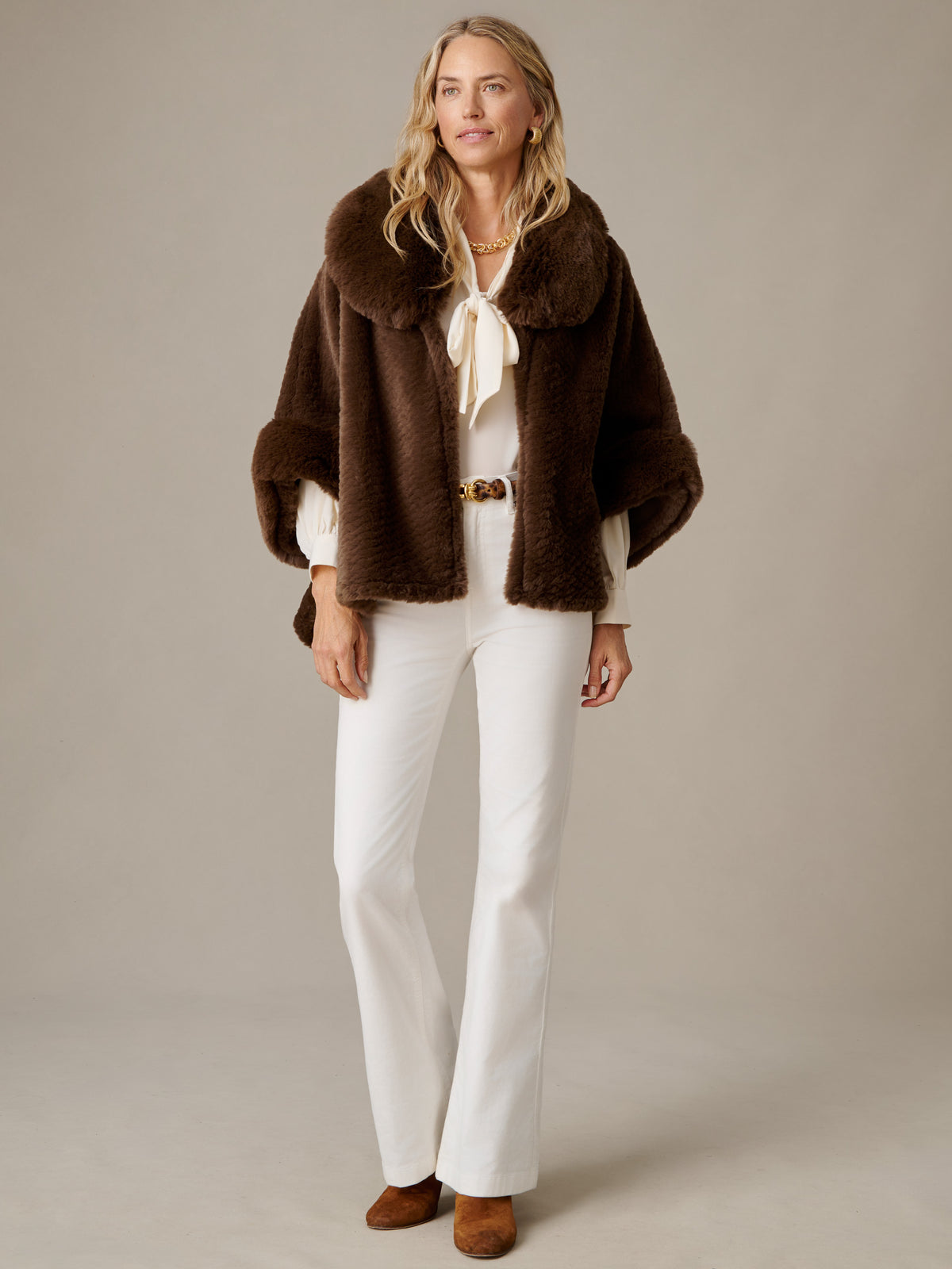 J.McLaughlin Andie Faux Fur Cape in brown faux fur styled over a white blouse and pants with brown boots for a timeless polished look