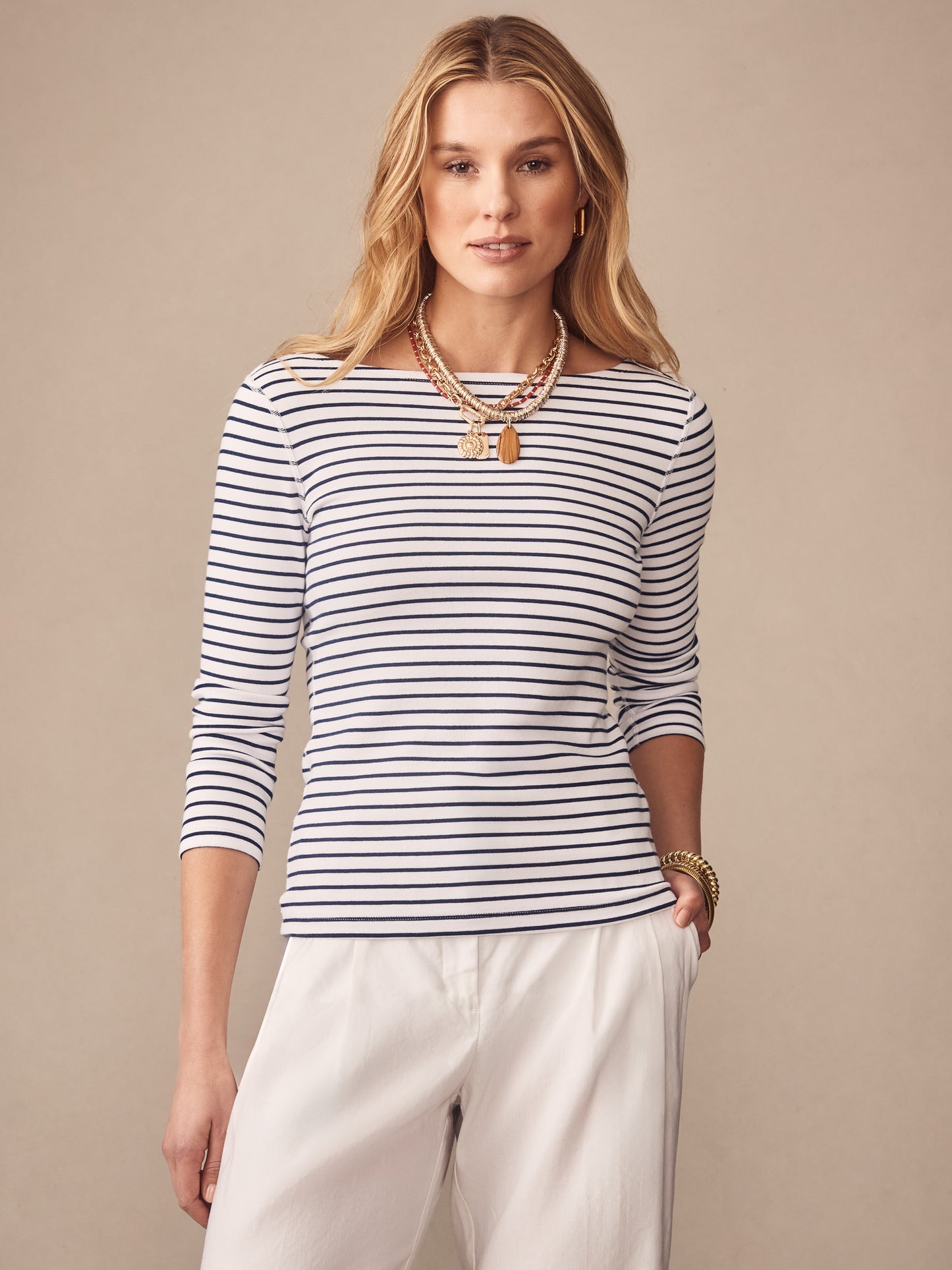 Woman wearing J.McLaughlin Goldie Tee in Stripe, a classic white and navy striped top paired with white pants, showcasing effortlessly stylish, enduring designs and innovative fabrics.
