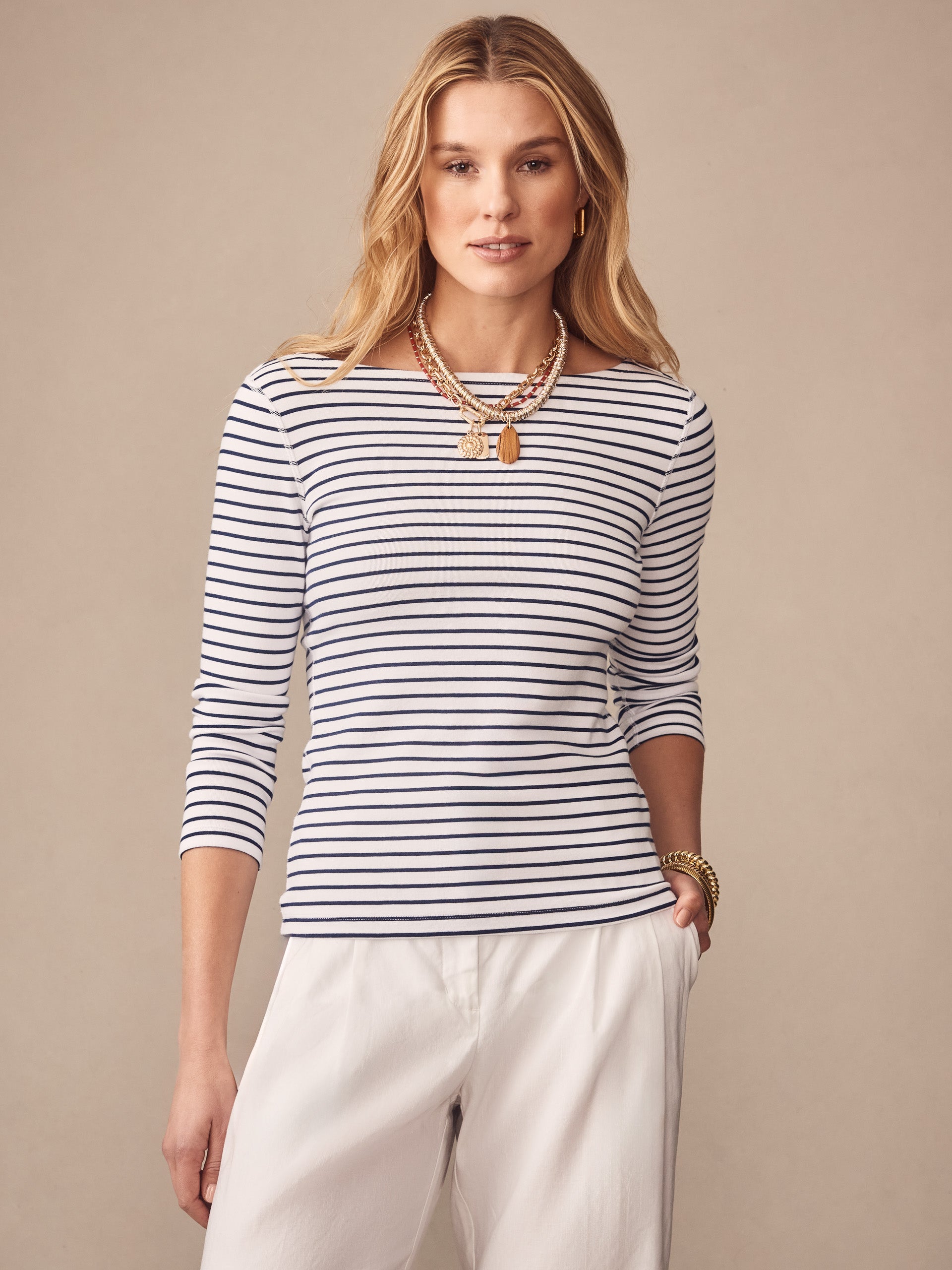 Woman wearing J.McLaughlin Goldie Tee in Stripe, a classic white and navy striped top paired with white pants, showcasing effortlessly stylish, enduring designs and innovative fabrics.
