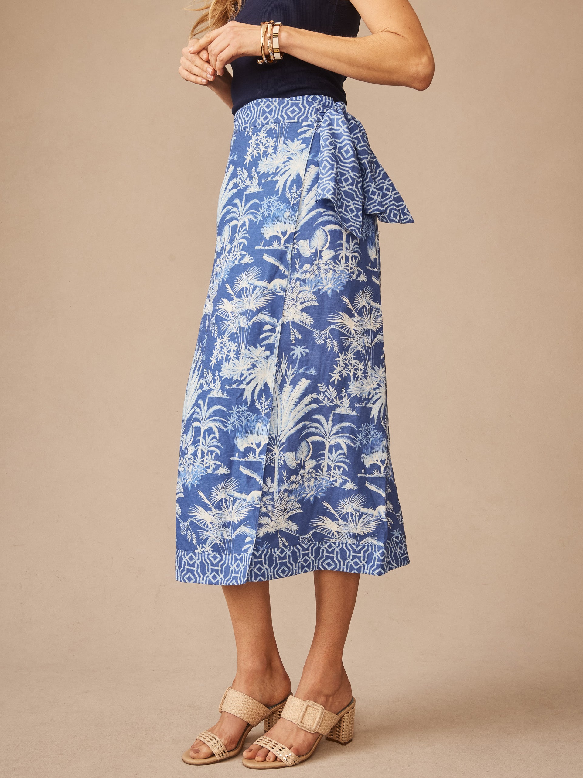 A side view of a woman wearing the Ardis Linen Blend Skirt in Garden Isle by J.McLaughlin, featuring a blue and white botanical print, paired with neutral heeled sandals and bracelets, showcasing effortlessly stylish, enduring designs with innovative fabrics from a destination for defining style. Life, Well-Lived.