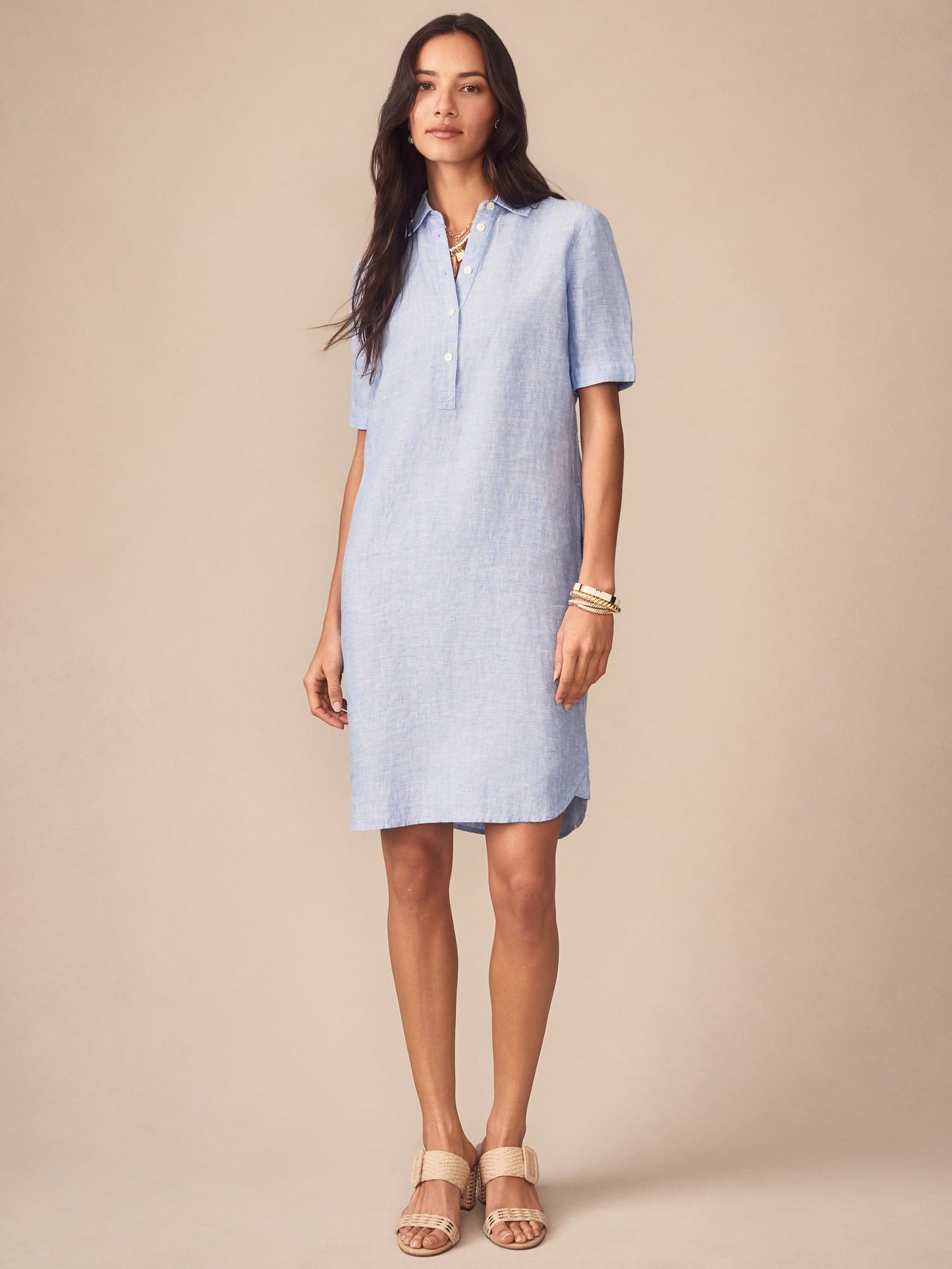 Woman wearing a light blue Arissa Linen Dress by J.McLaughlin, styled with neutral sandals and bracelets, showcasing effortlessly stylish, enduring designs and a legacy of timeless fashion.