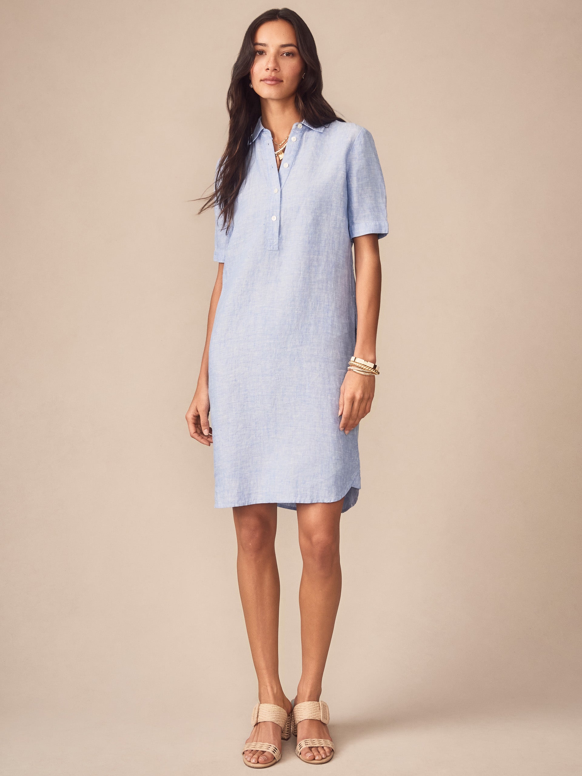 Woman wearing a light blue Arissa Linen Dress by J.McLaughlin, styled with neutral sandals and bracelets, showcasing effortlessly stylish, enduring designs and a legacy of timeless fashion.