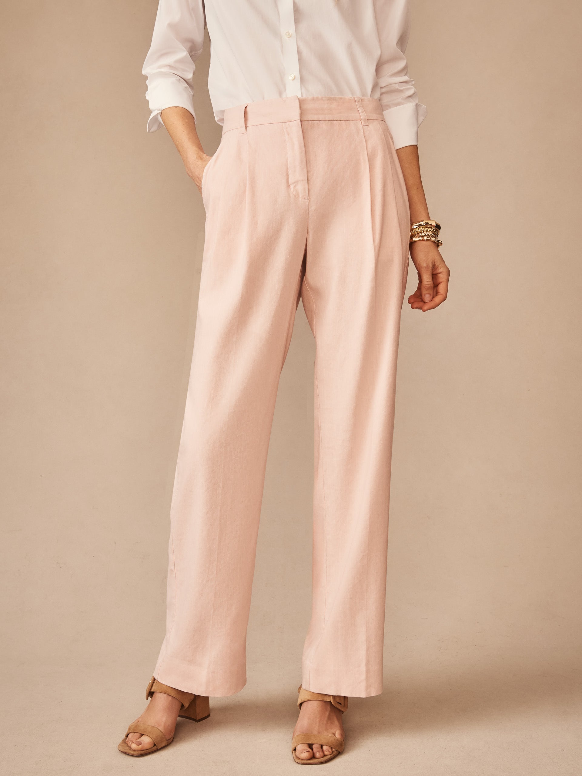 Woman wearing light pink Fiona Linen Blend Pants paired with a white button-up shirt and tan block-heeled sandals, showcasing effortlessly stylish and enduring designs by J.McLaughlin.